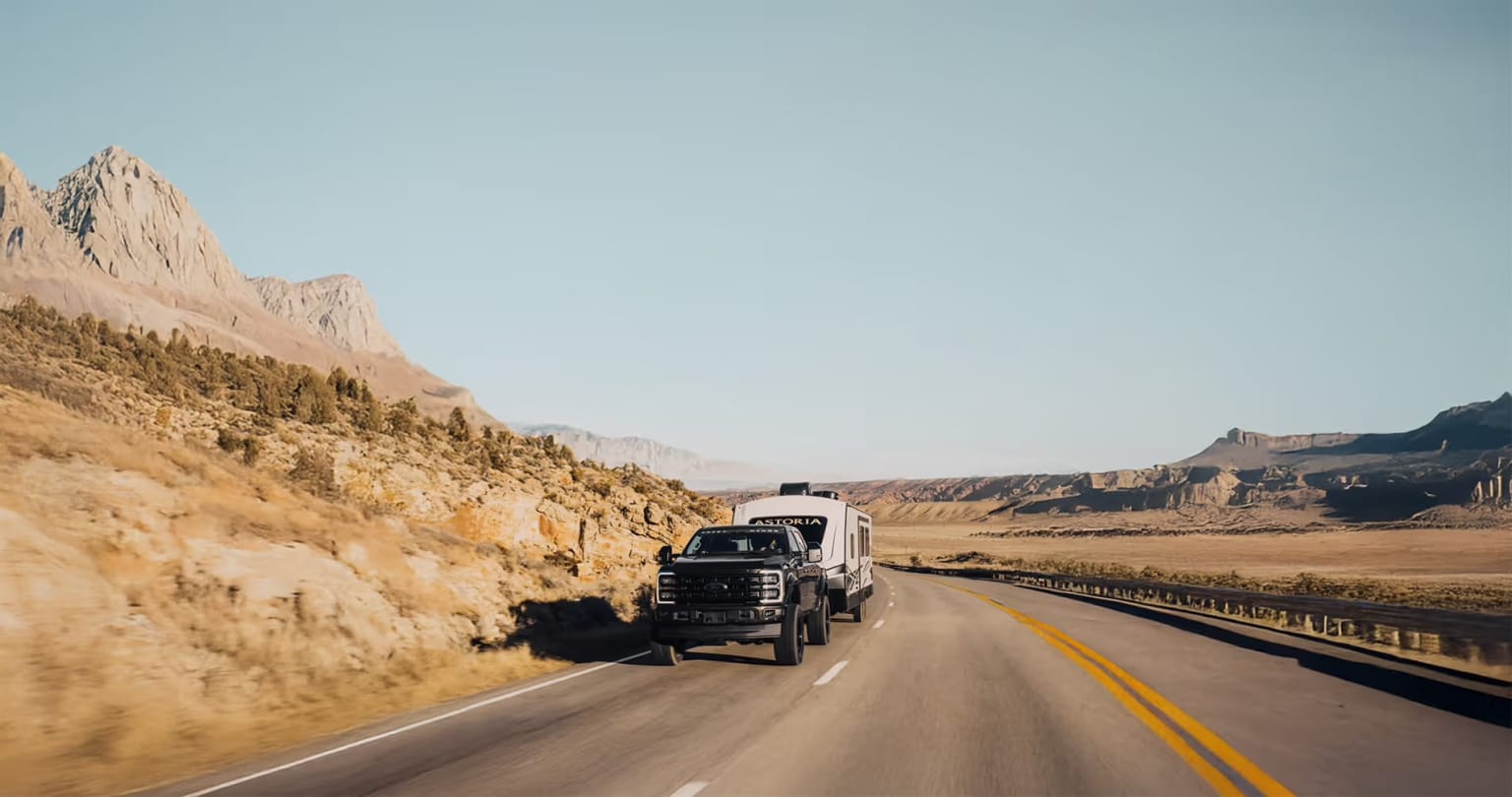 A large semi-truck navigating a winding mountain road with rocky cliffs and a desert landscape in the background.