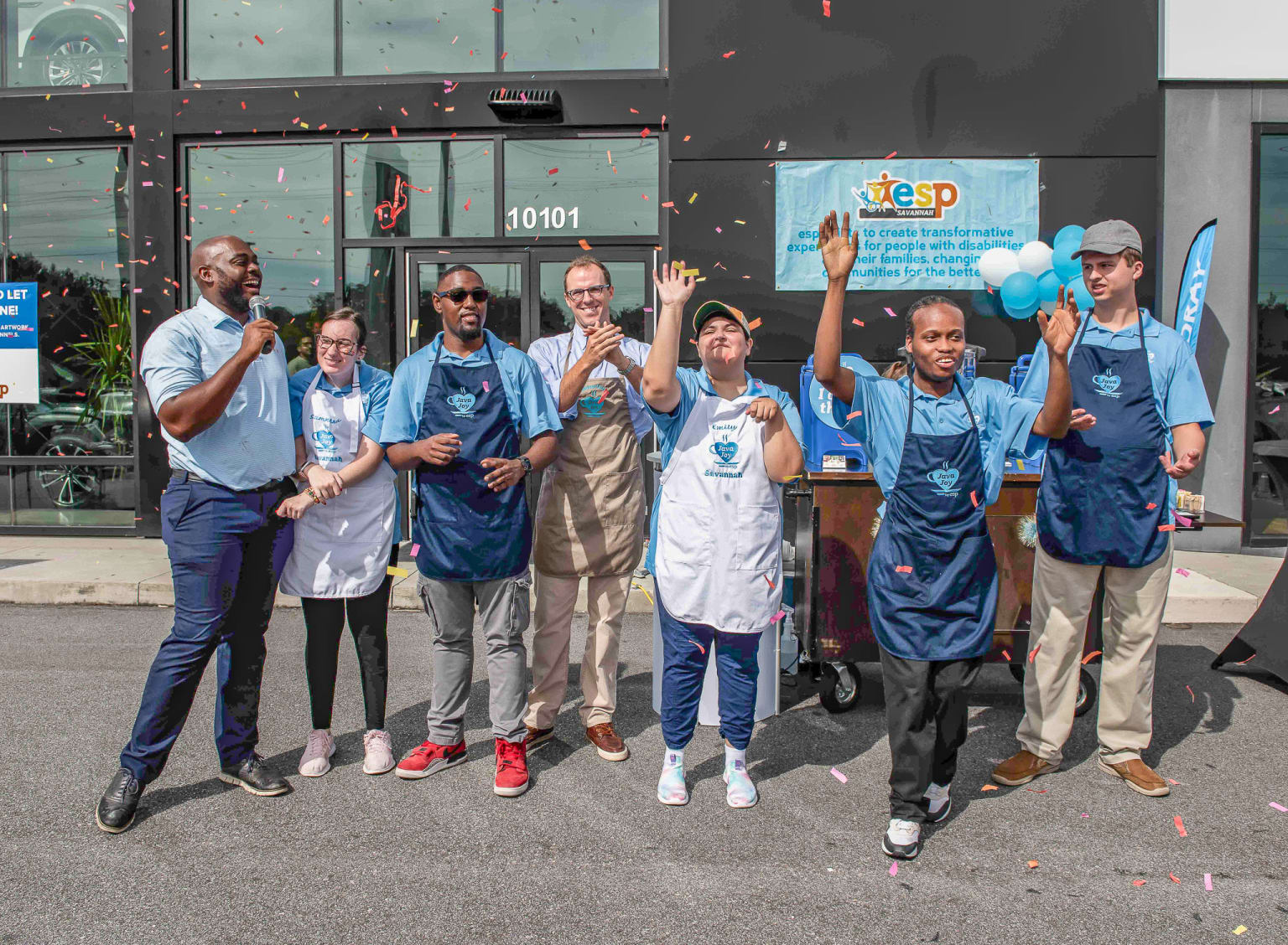 A group of people in blue uniforms, some holding blue balloons, standing in front of a building with the number "10101" displayed.