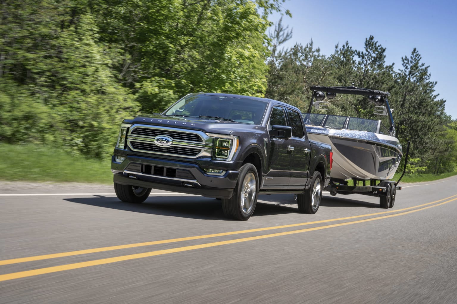 a black truck pulling a boat on the back of it's trailer on a road with trees in the background
