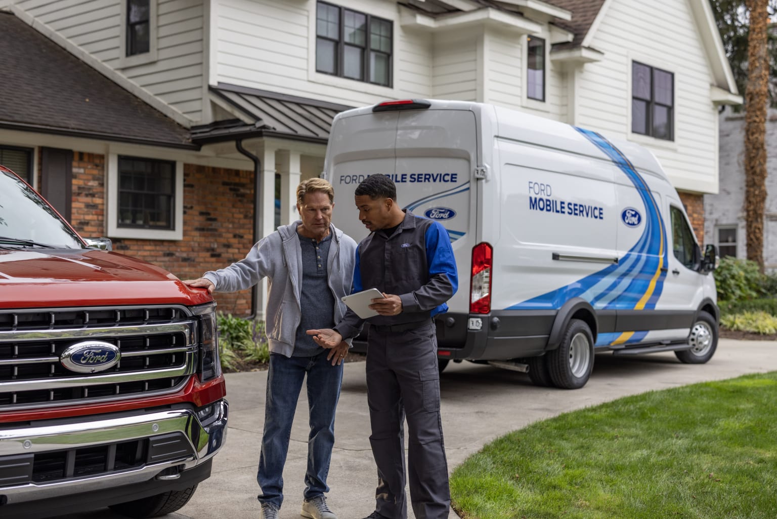 Two men in casual attire standing next to a service van parked in front of a residential house with a well-manicured lawn.