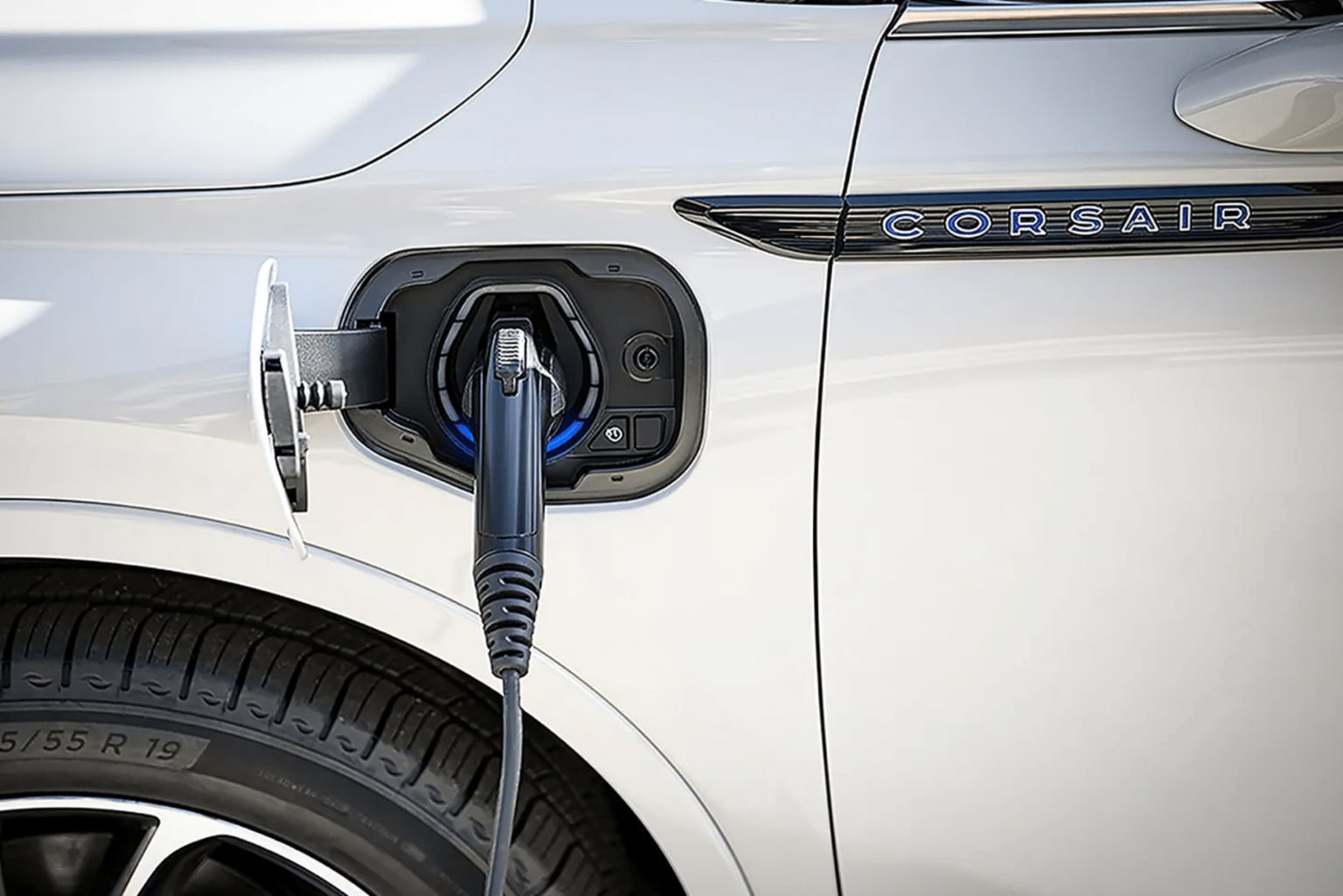 An electric vehicle is being charged using a charging cable plugged into the vehicle's charging port, with the background showing a blurred environment.