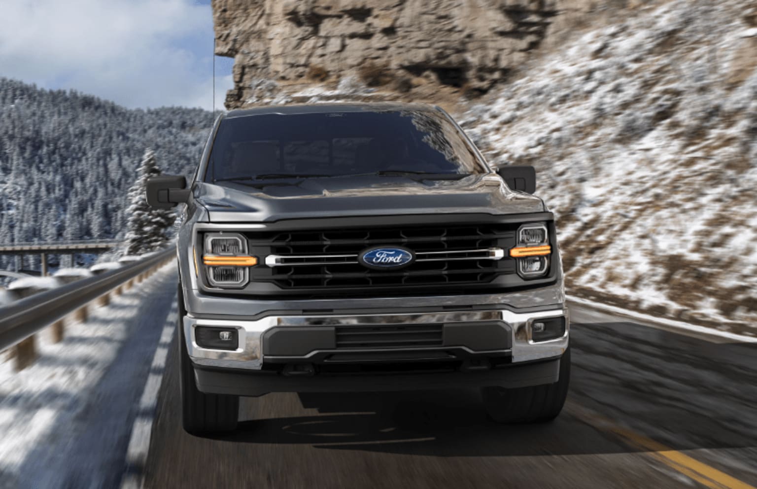A rugged pickup truck navigates a snowy mountain road, with a towering cliff face in the background.