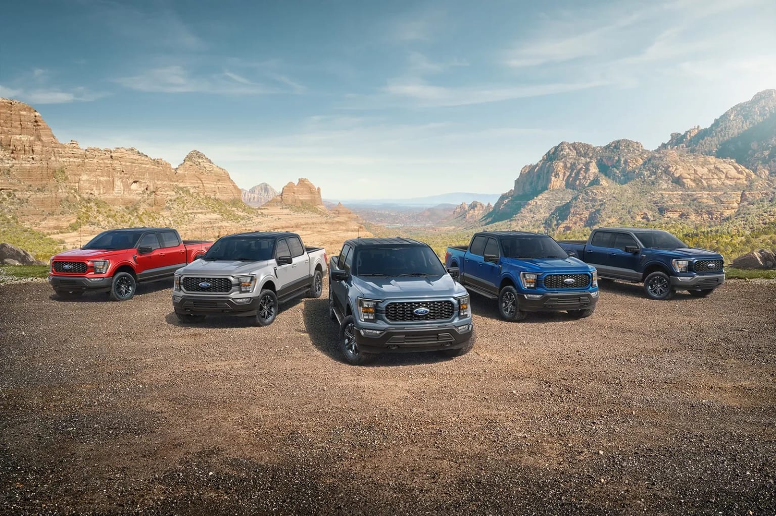 a group of four pickup trucks parked in front of a mountain range in a desert area with mountains in the background