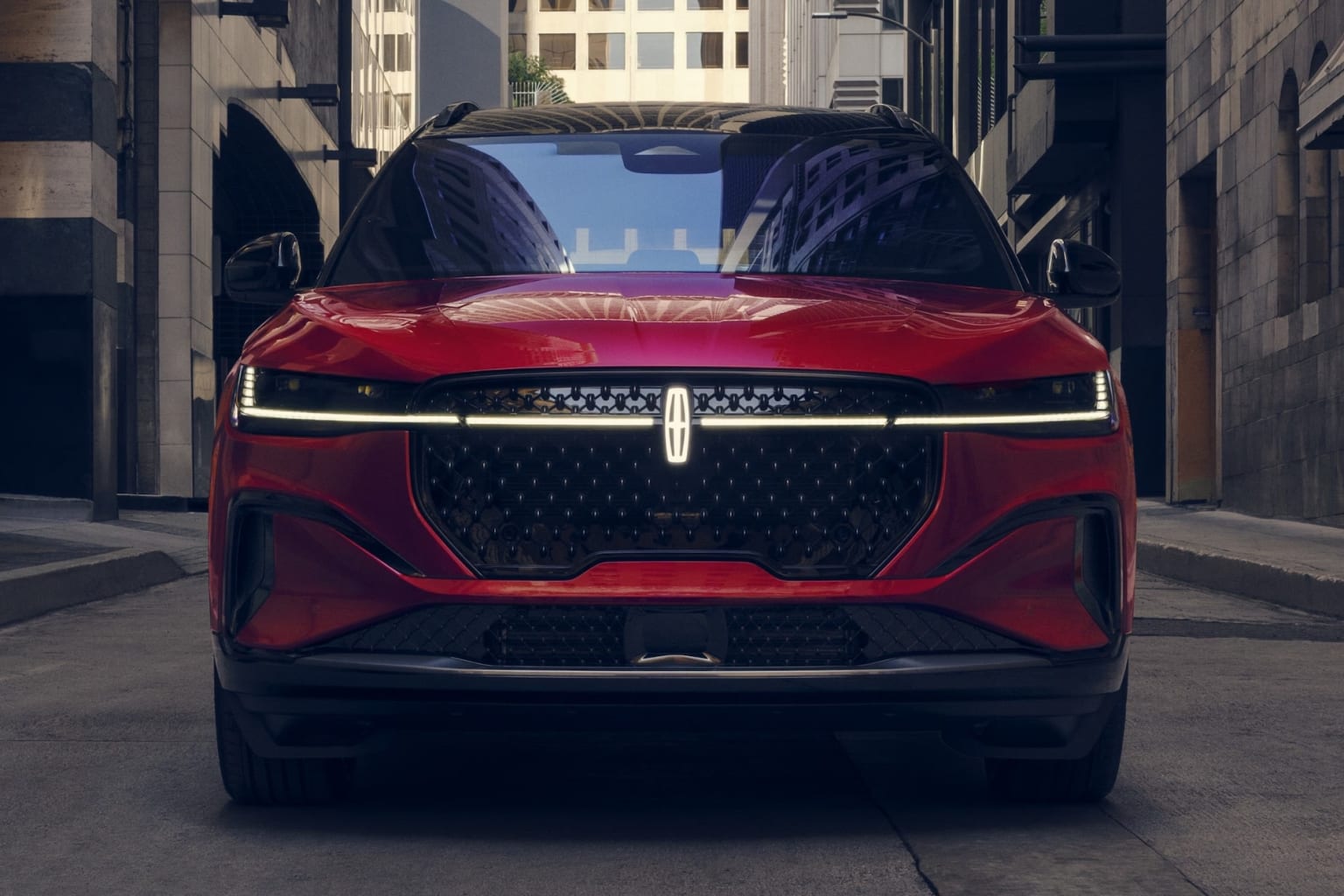 A sleek, red luxury SUV parked in a narrow urban alley, surrounded by tall buildings in a dimly lit environment.