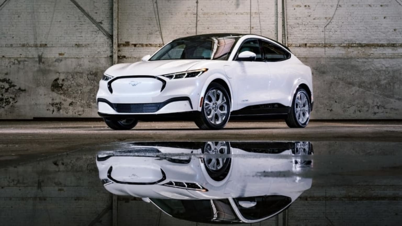 a white car is parked in front of a brick wall and reflecting in the water of a pool of water