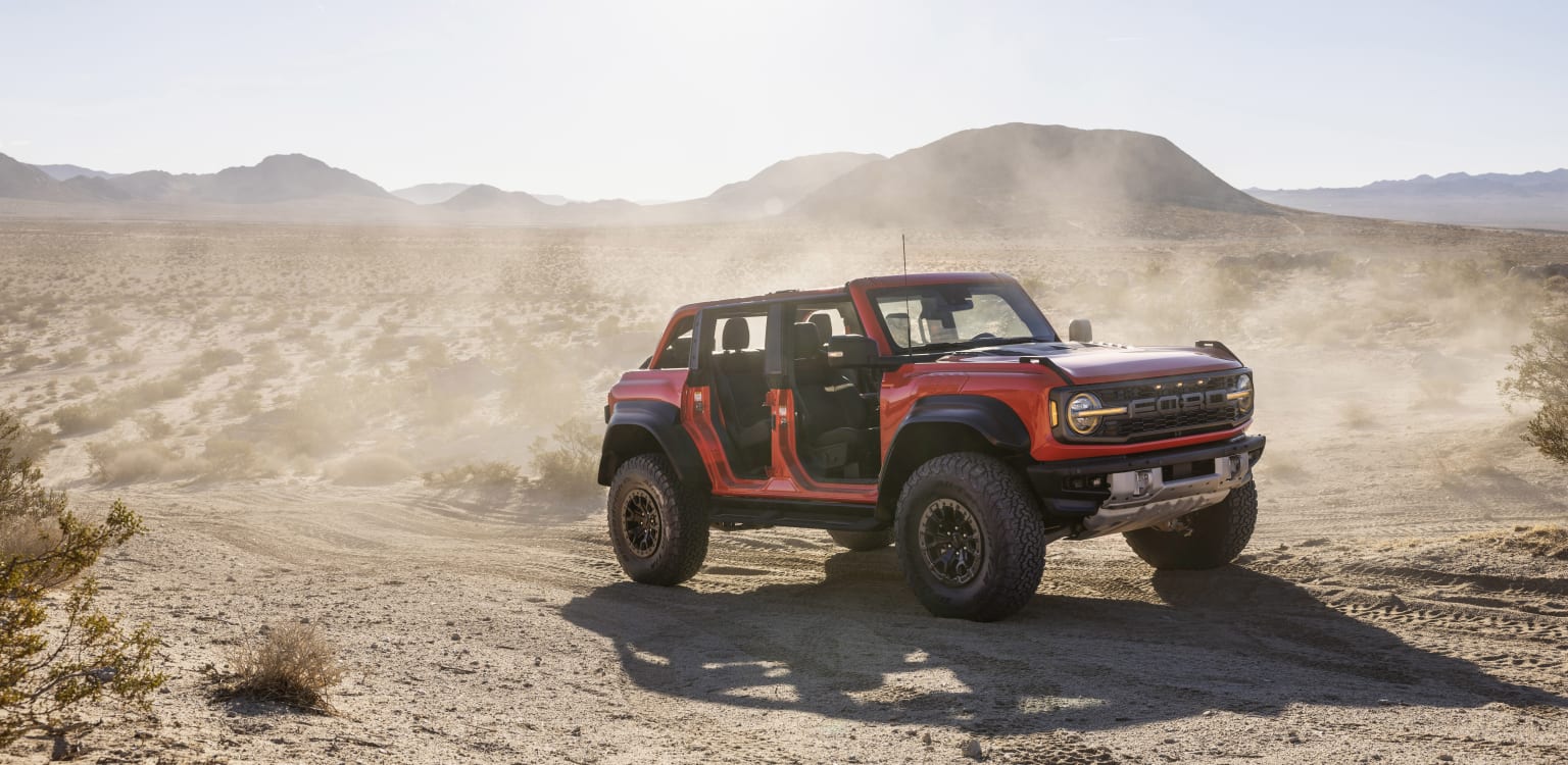 a red truck driving down a dirt road in the middle of a desert area with mountains in the background