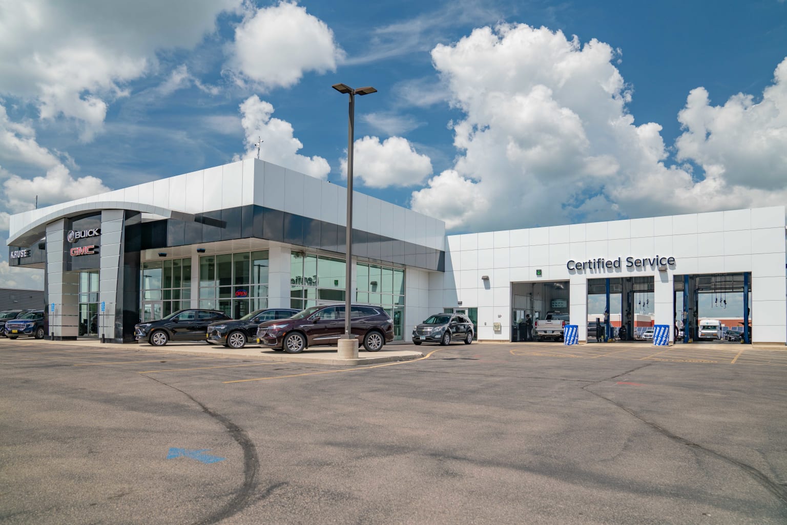 a car dealership with several cars parked in front of it and clouds in the sky over the parking lot