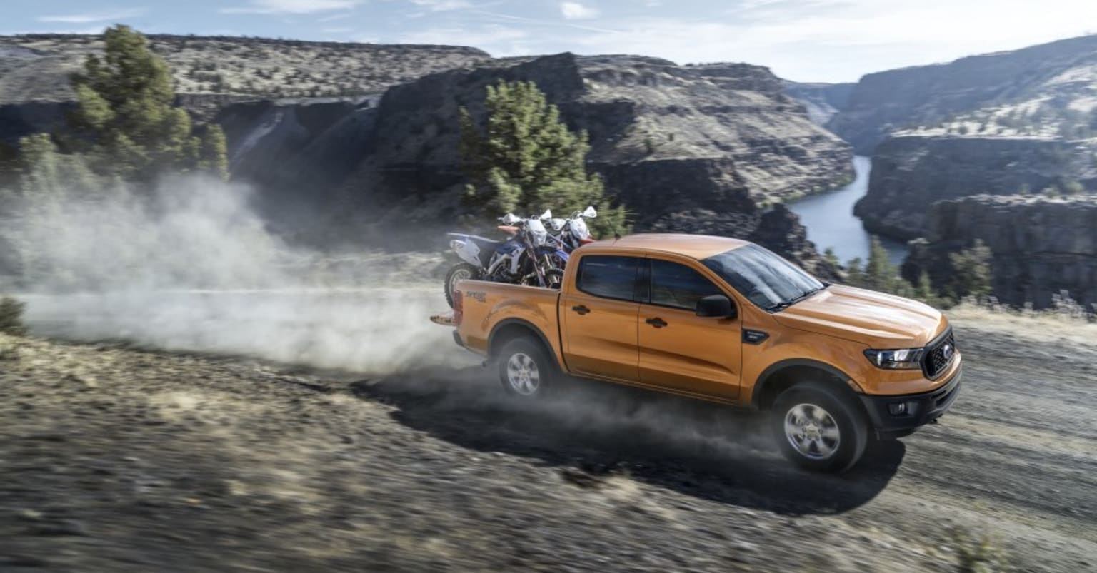 a pick up truck driving down a dirt road in the mountains with a group of people on the back of it