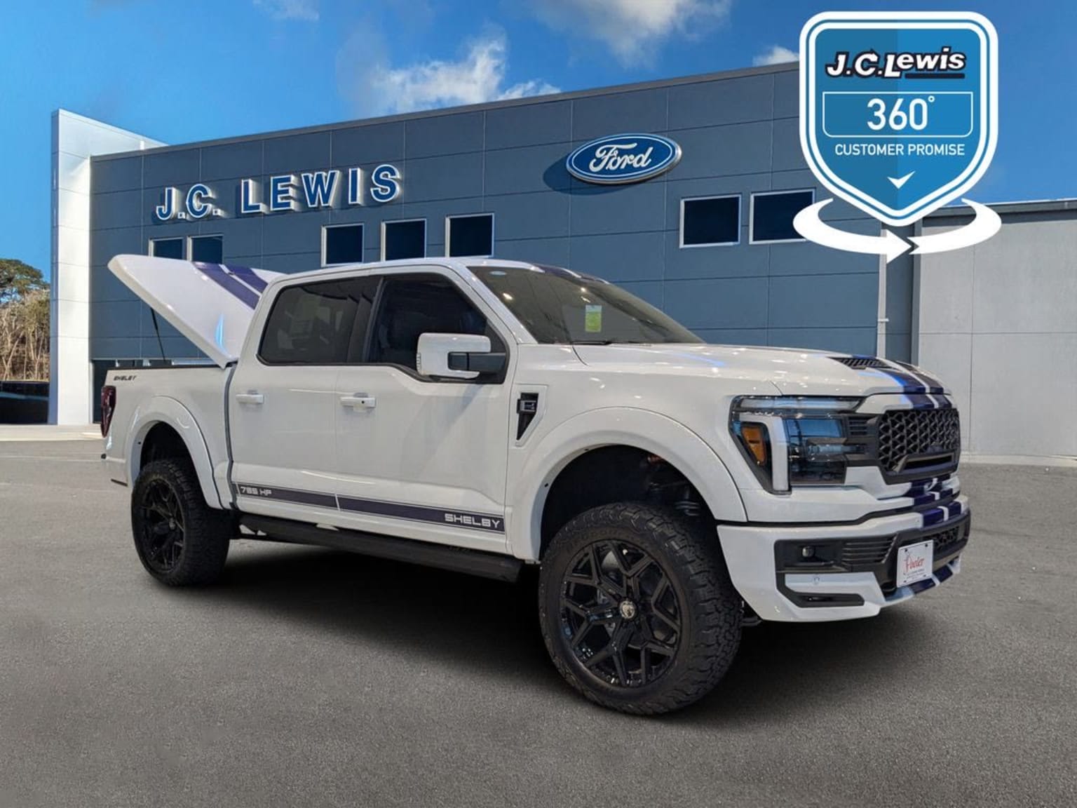 A white pickup truck is prominently displayed in the foreground, parked in front of a dealership building with a logo visible in the background.