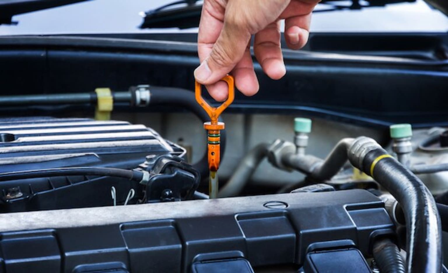 a person holding a wrench in front of a car's engine bay with the hood open and the hood up