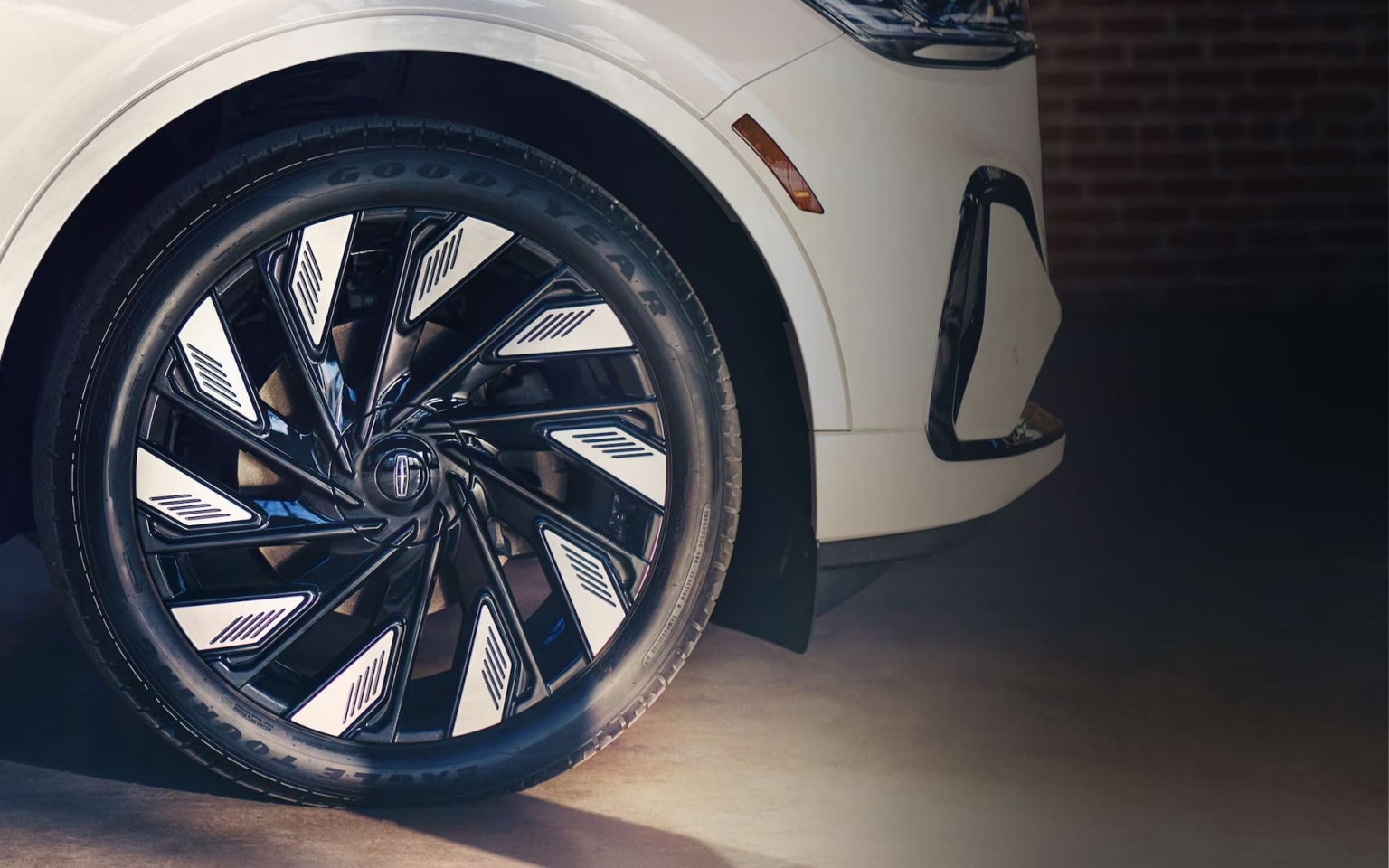 Close-up view of a car's wheel with a sleek and modern design featuring intricate patterns on the alloy rim, set against a plain, light-colored surface.
