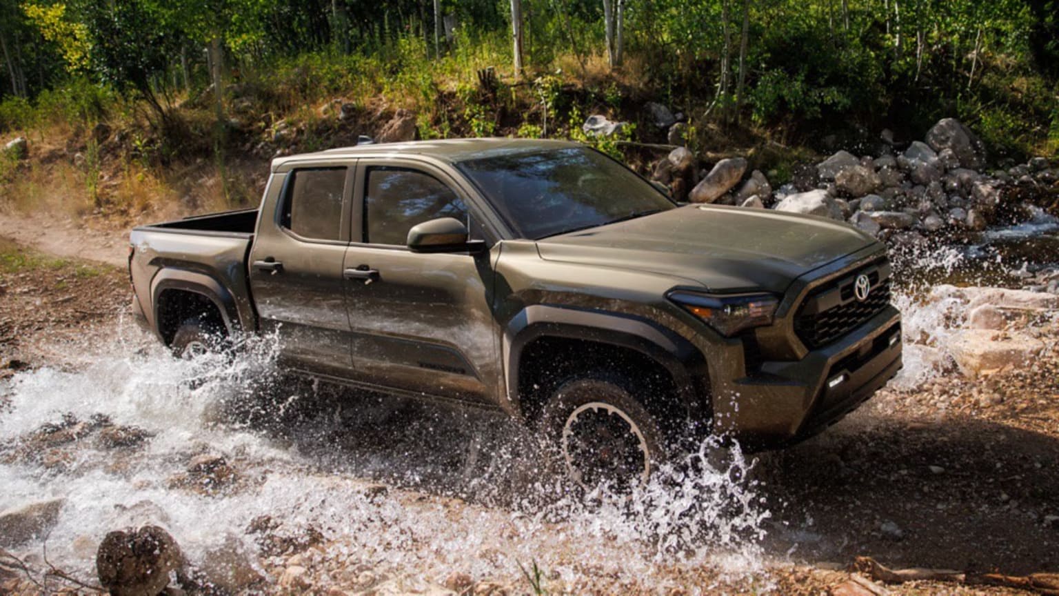 Off-road pickup truck crossing a shallow stream in a forested environment.