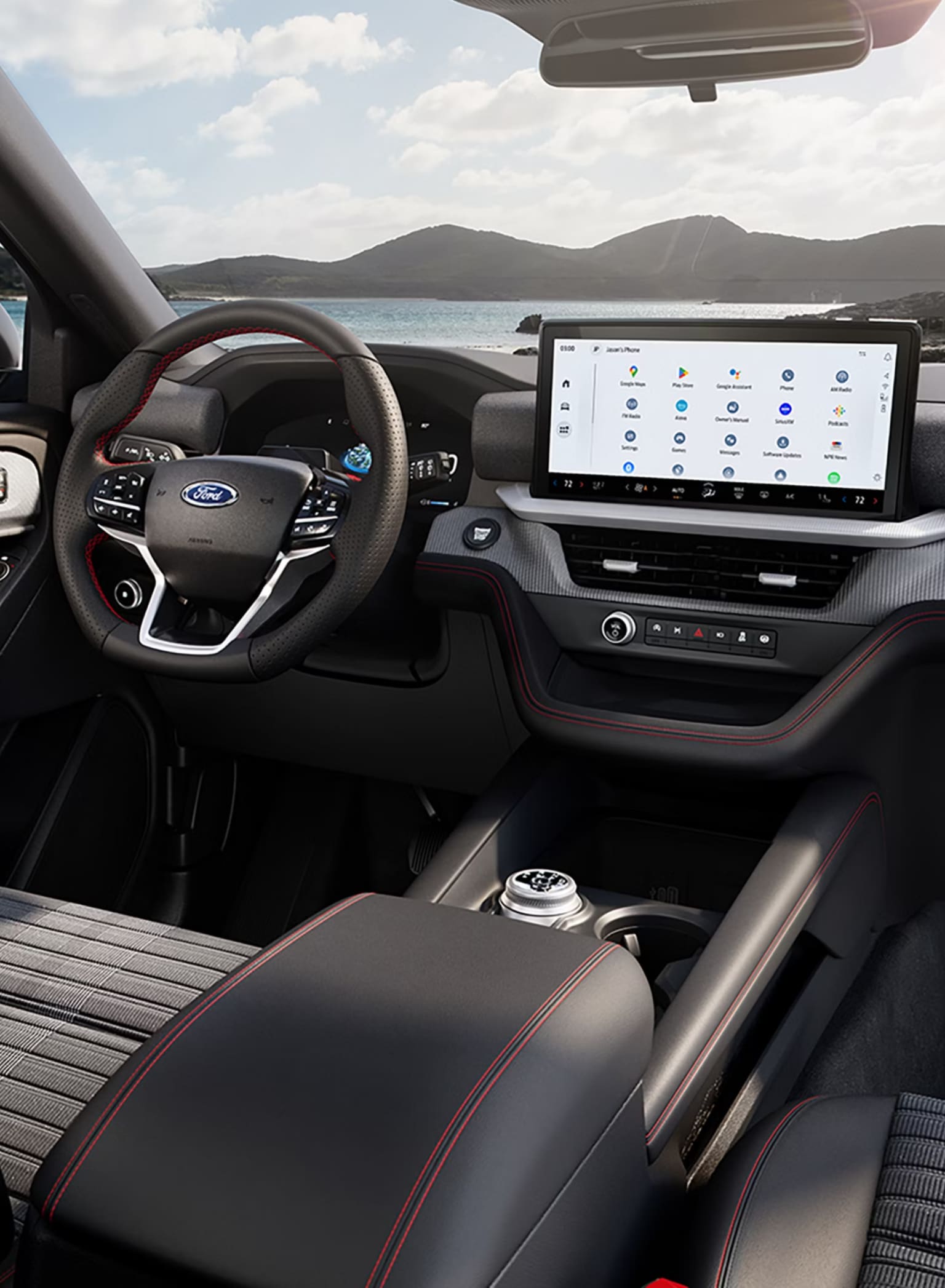 The interior of a modern vehicle with red stitching and a large digital display, set against a scenic background of mountains and a body of water.