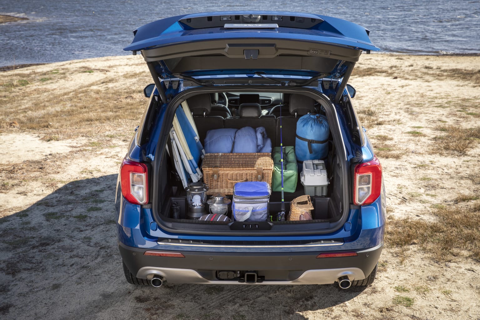 the back end of a blue van with luggage in the trunk and a lake in the distance in the background