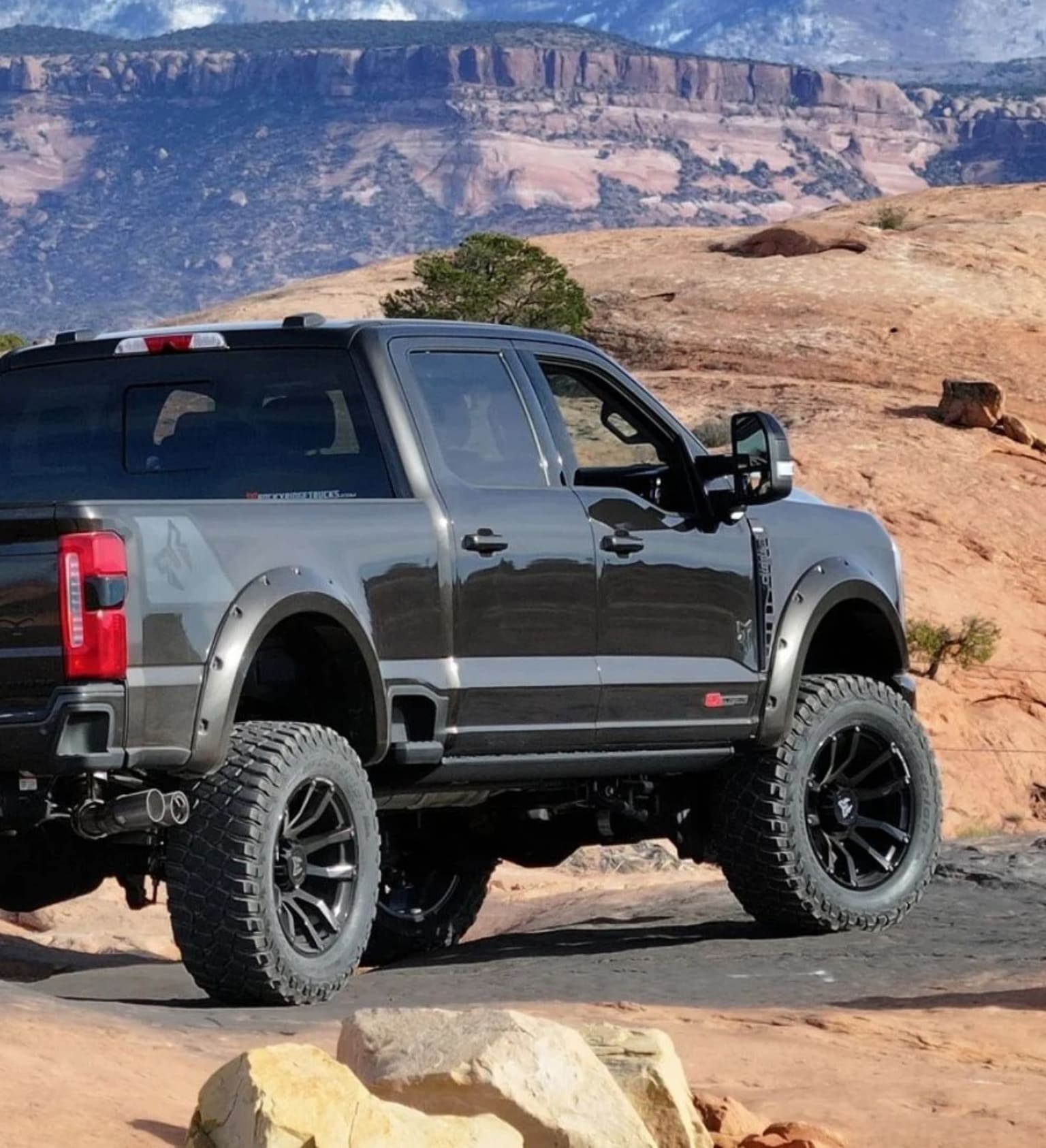 Off-road pickup truck in rugged landscape with cliffs and mountains in the background.