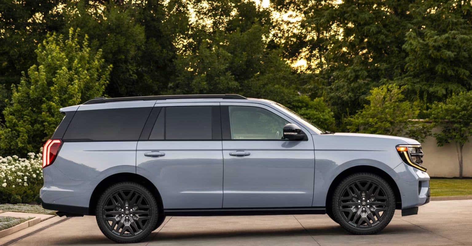 White SUV parked on a driveway with greenery and trees in the background.