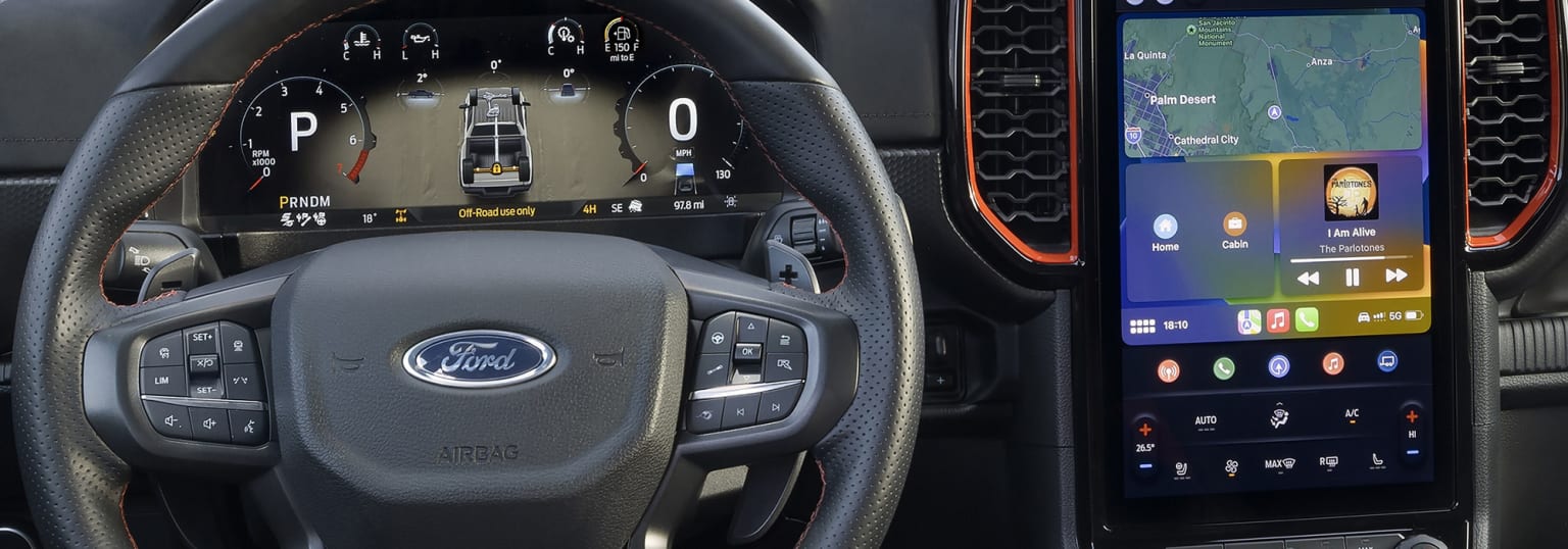 Interior of a vehicle with steering wheel, dashboard, controls, displays, and navigation system screen.