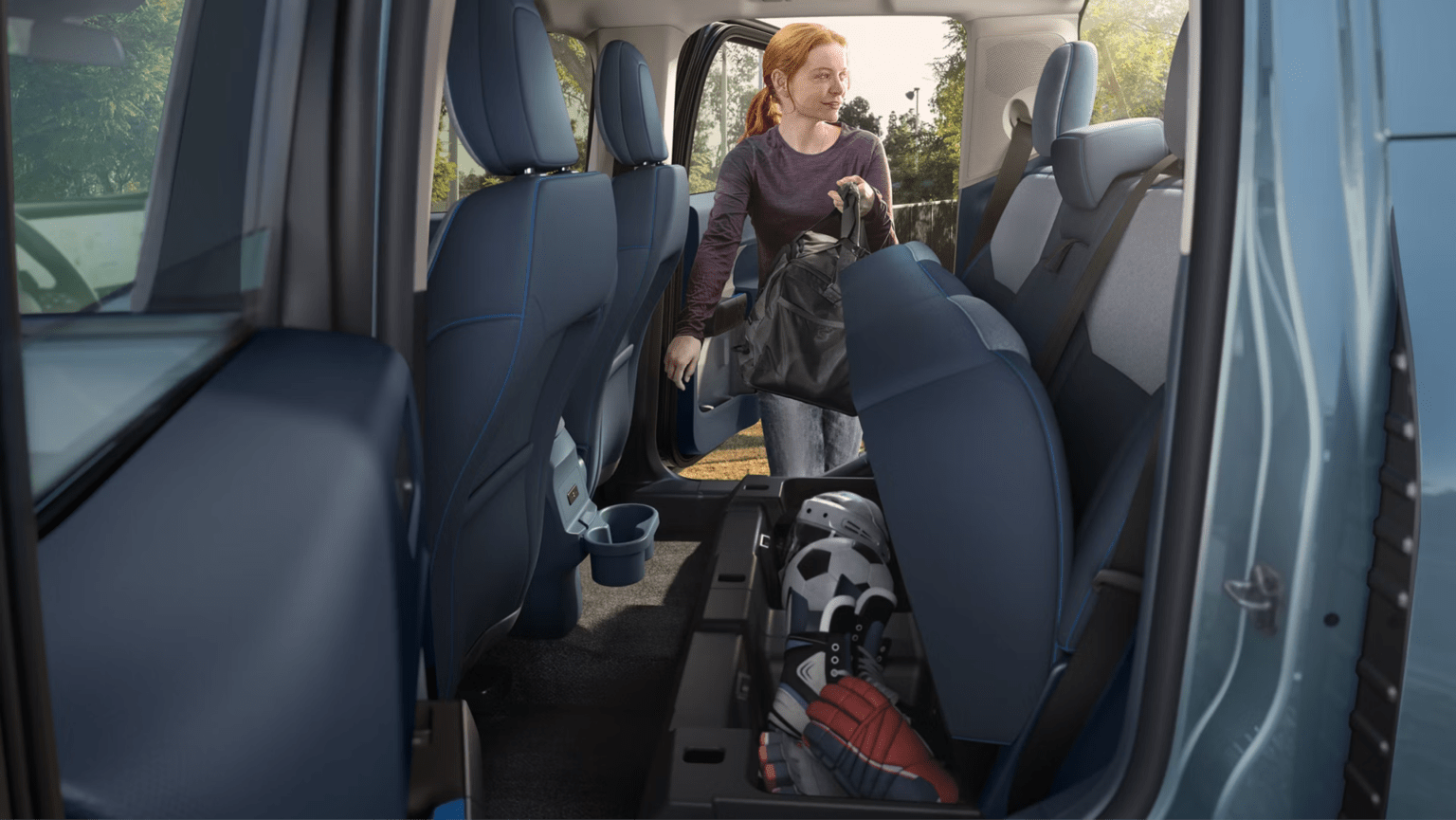 A person loads sports equipment into the roomy interior of a vehicle, with trees and a fence visible in the sunlit background.