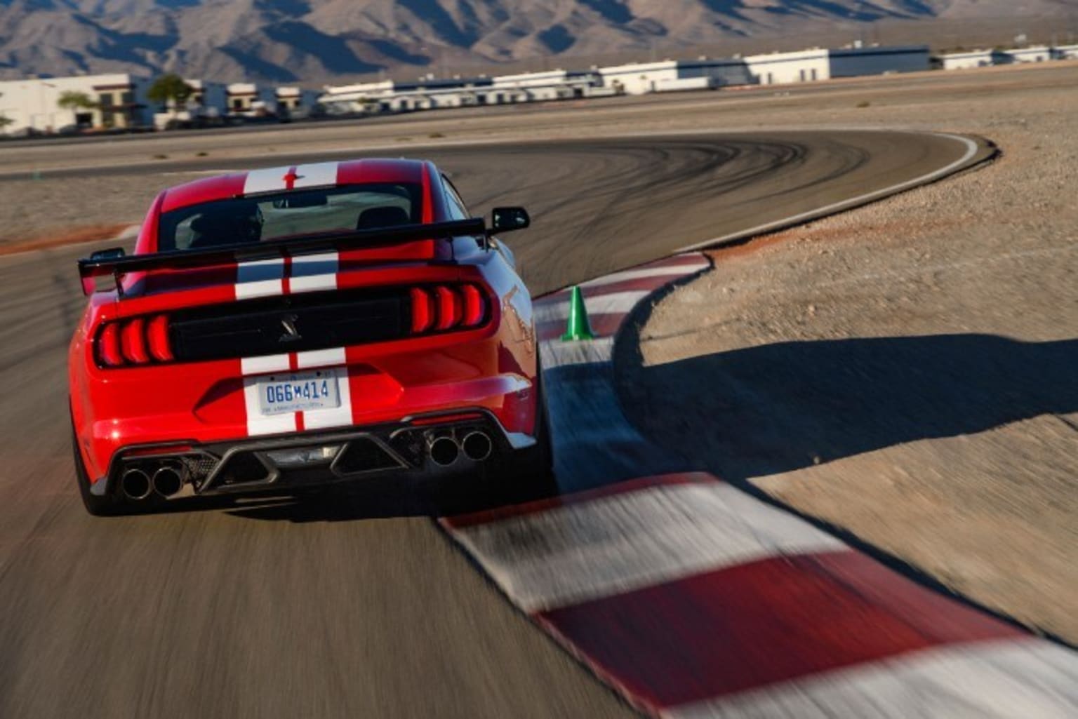 a red sports car driving on a race track with mountains in the background of the picture