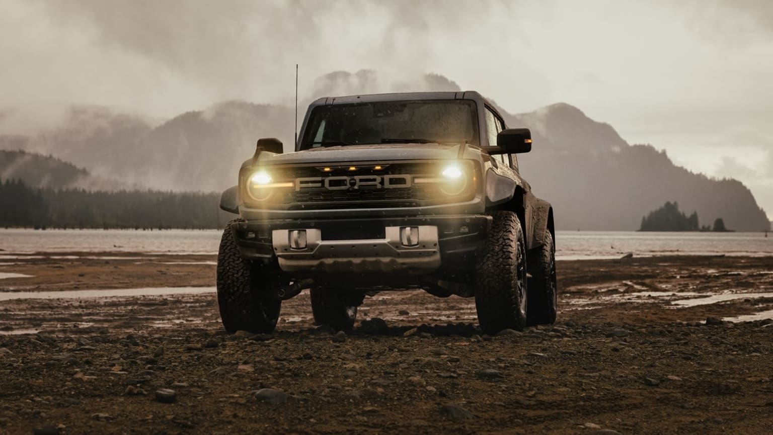An off-road vehicle with headlights on, against a misty mountainous background.