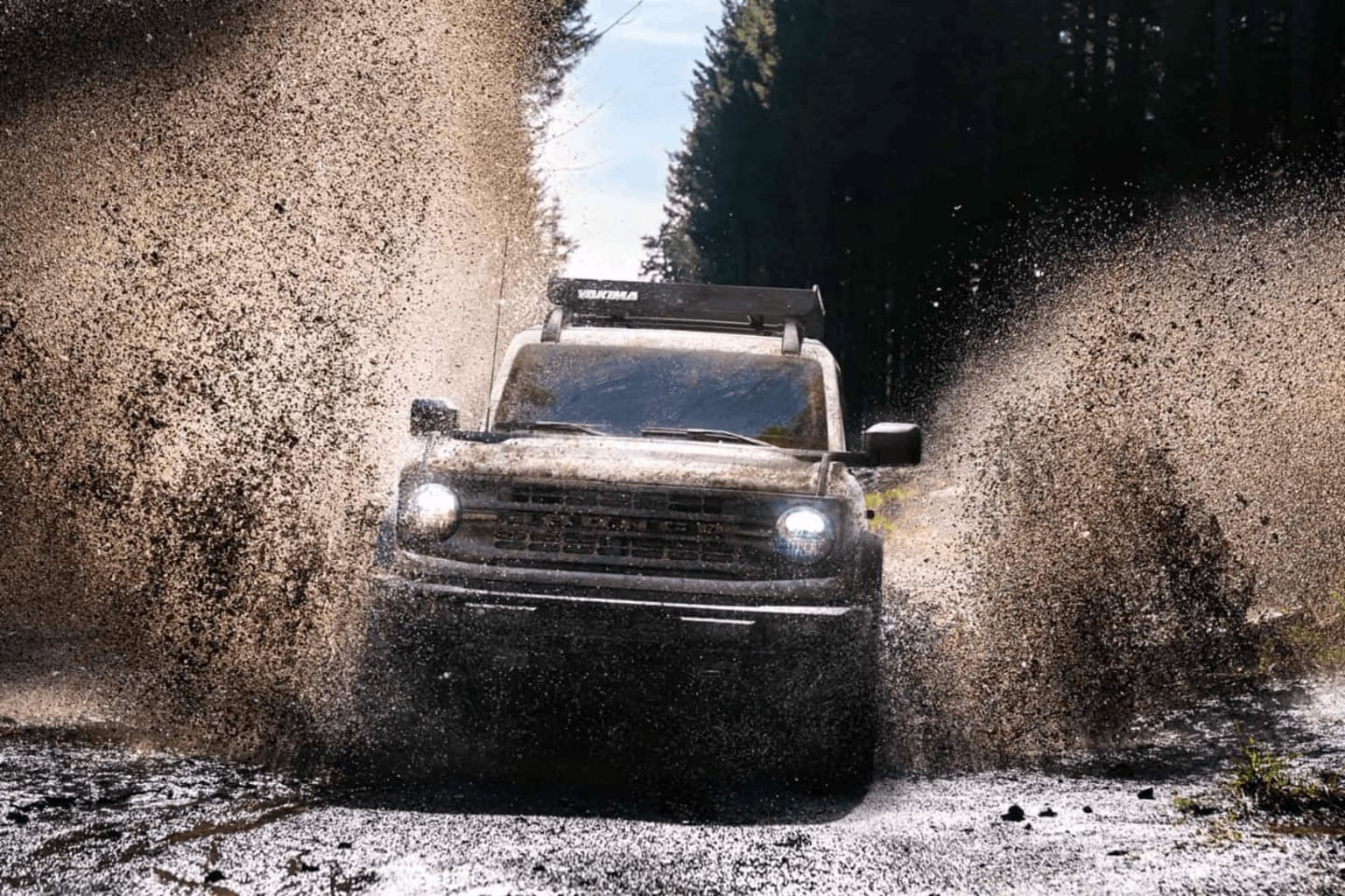 a truck is driving through a mud puddle in the mud on a dirt road with trees in the background