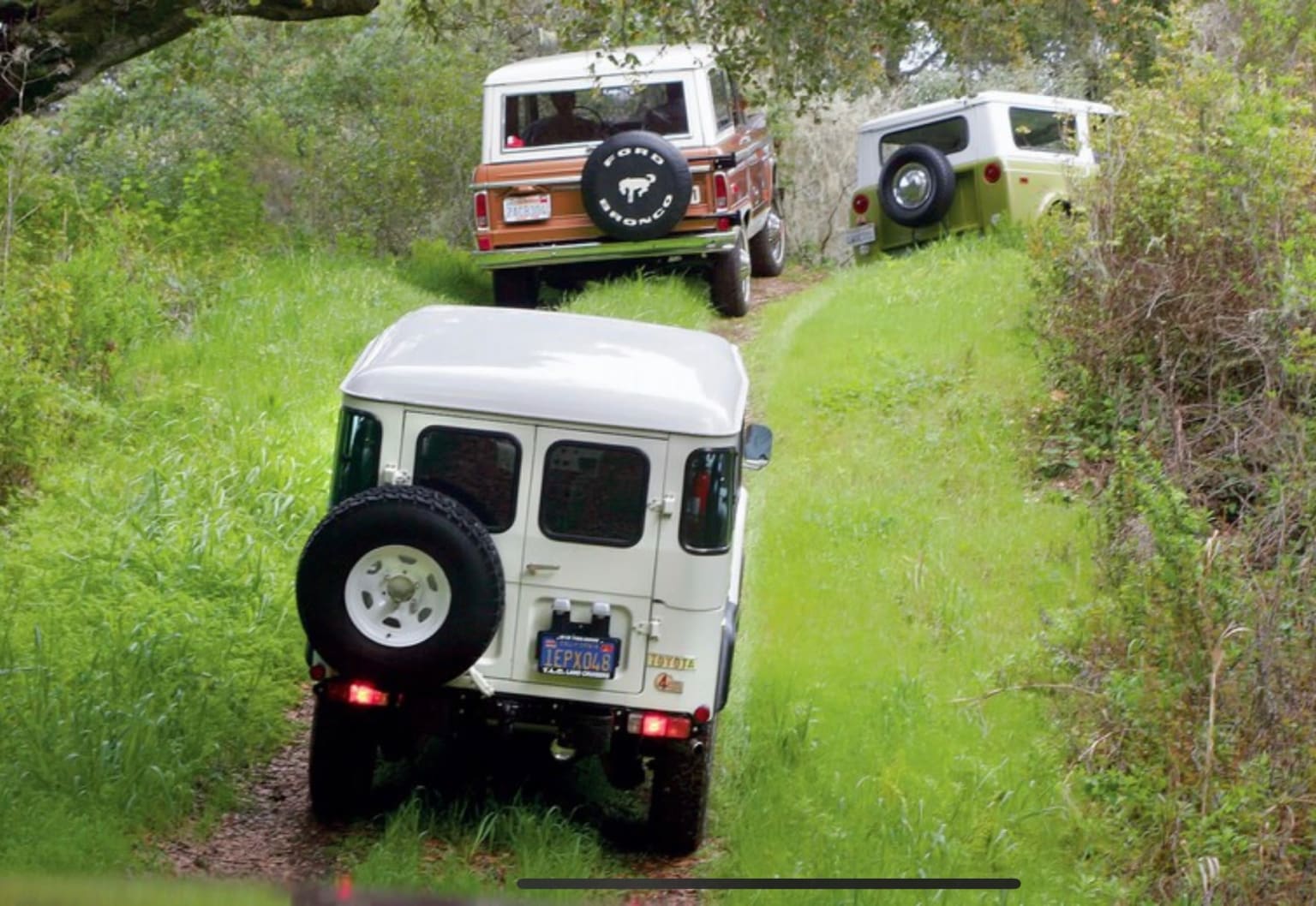 a jeep driving down a dirt road next to another jeep driving down a dirt road next to a lush green field