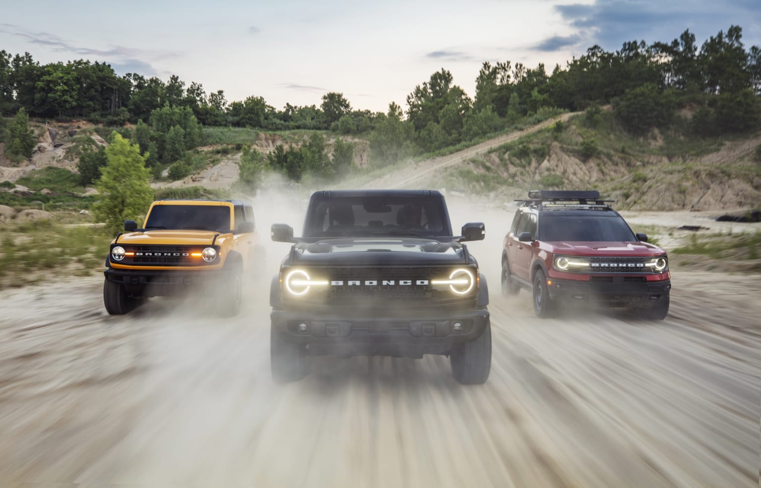 three jeeps driving on a dirt road in the woods at sunset or sunrise or dusk, with the headlights on and the front lights on