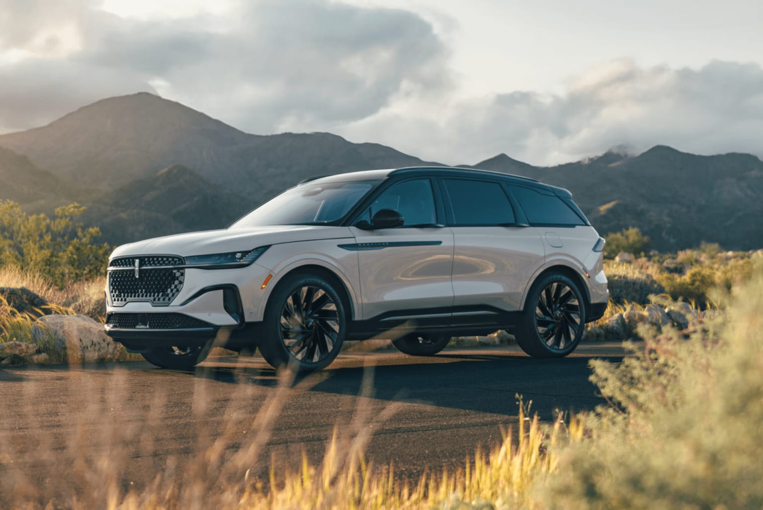 SUV in a field with mountains and cloudy skies in the background.