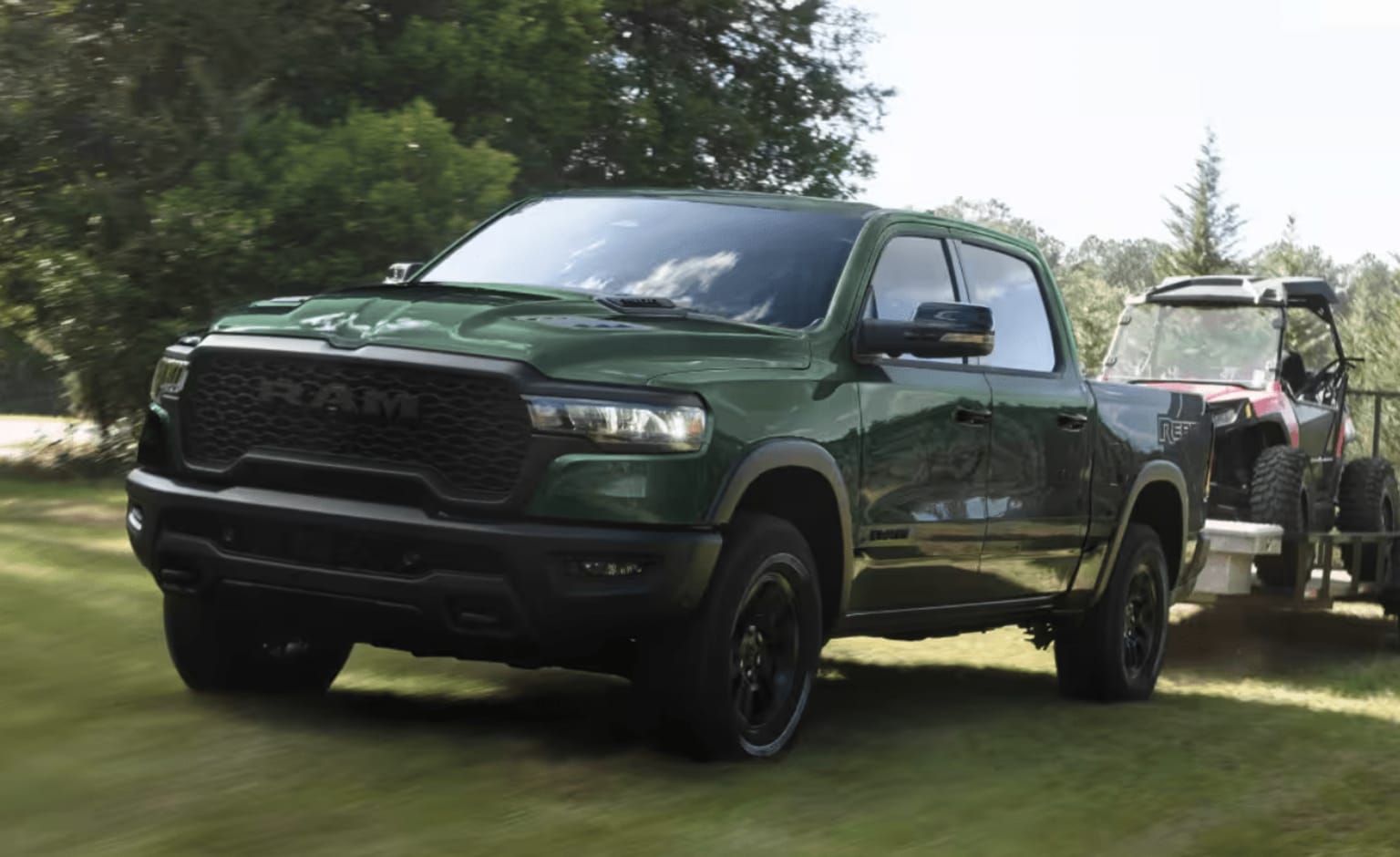 A large, rugged green pickup truck parked in a grassy, forested area with trees and foliage visible in the background.