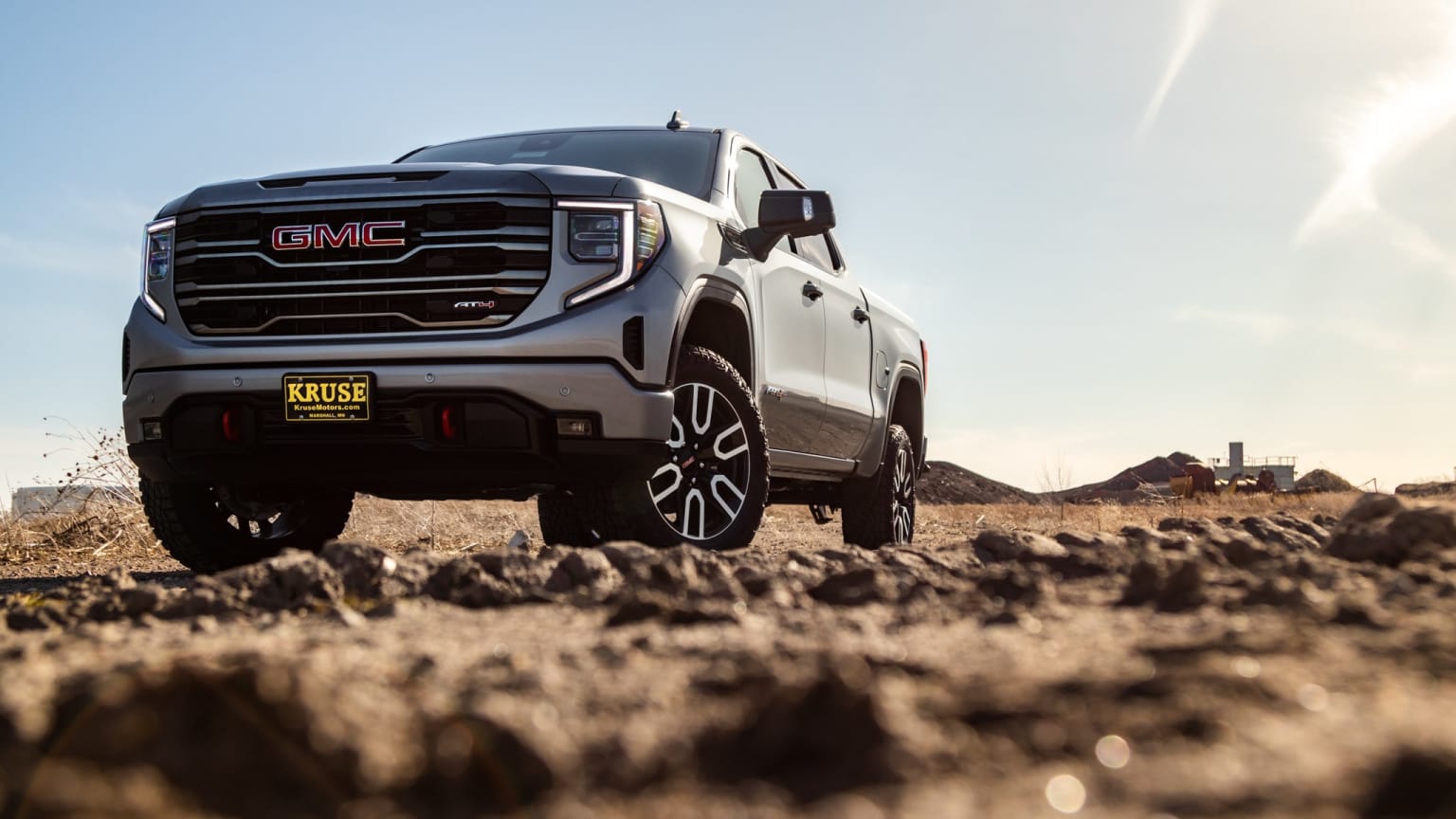 a white truck driving on a dirt road in the middle of a desert area with sun shining on the ground