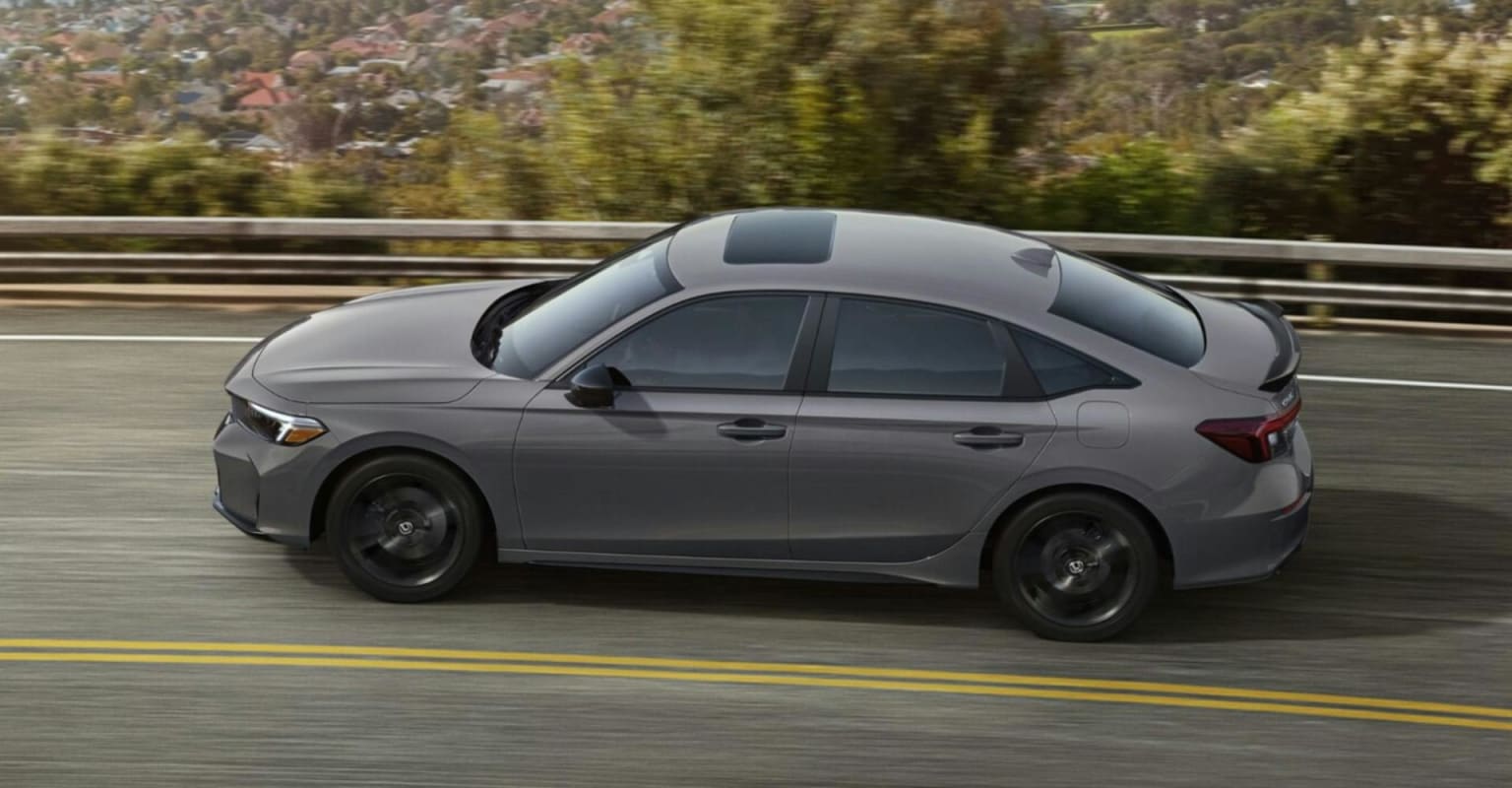 A gray sedan driving on a winding road with blurred trees and hills in the background.