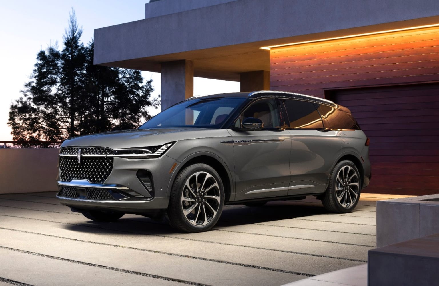A large, sleek gray SUV in front of a modern building with a beautiful sunset in the background.