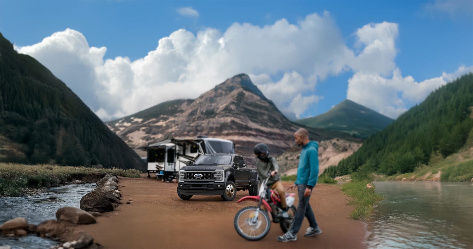 Off-road vehicle on dirt path by river, person on bicycle in foreground, mountains and dramatic clouds in background.