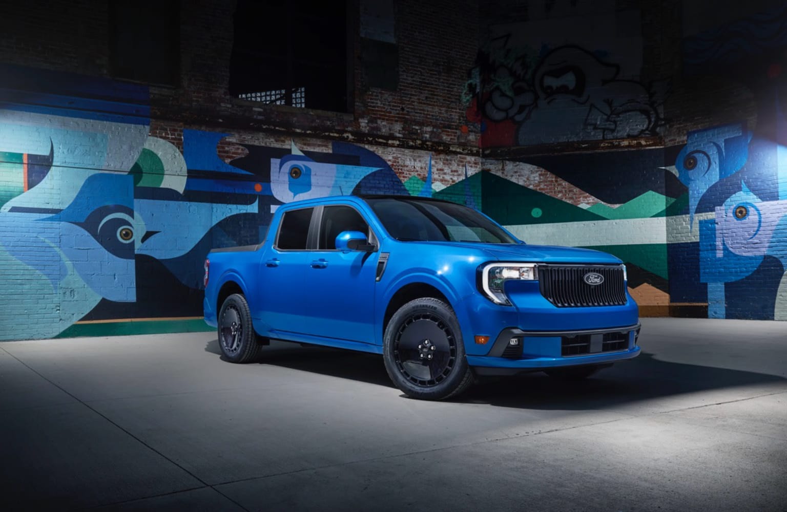 A bright blue pickup truck is parked in front of a vibrant, colorful mural on a brick wall.