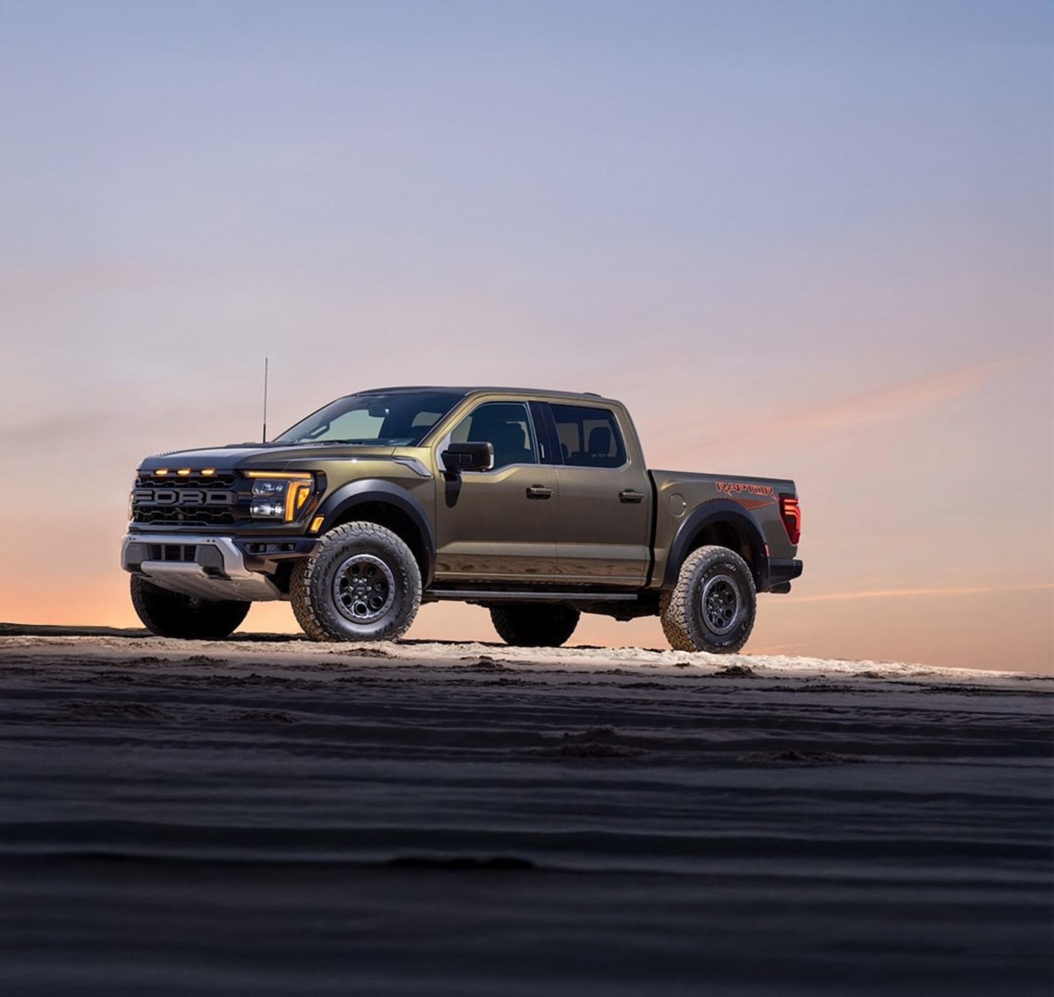 A rugged, off-road pickup truck in a flat, barren landscape with a vibrant sunset sky.