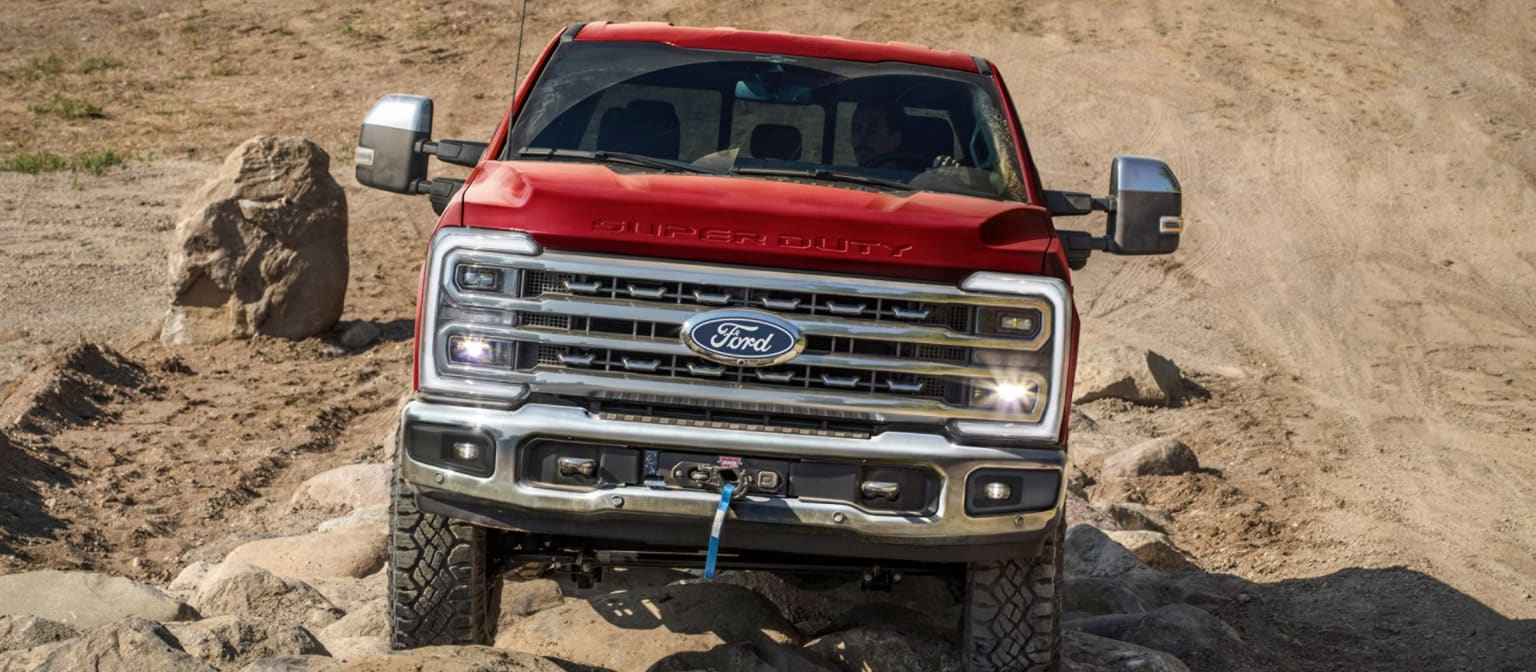 Red truck on rocky terrain with sandy hill in background.