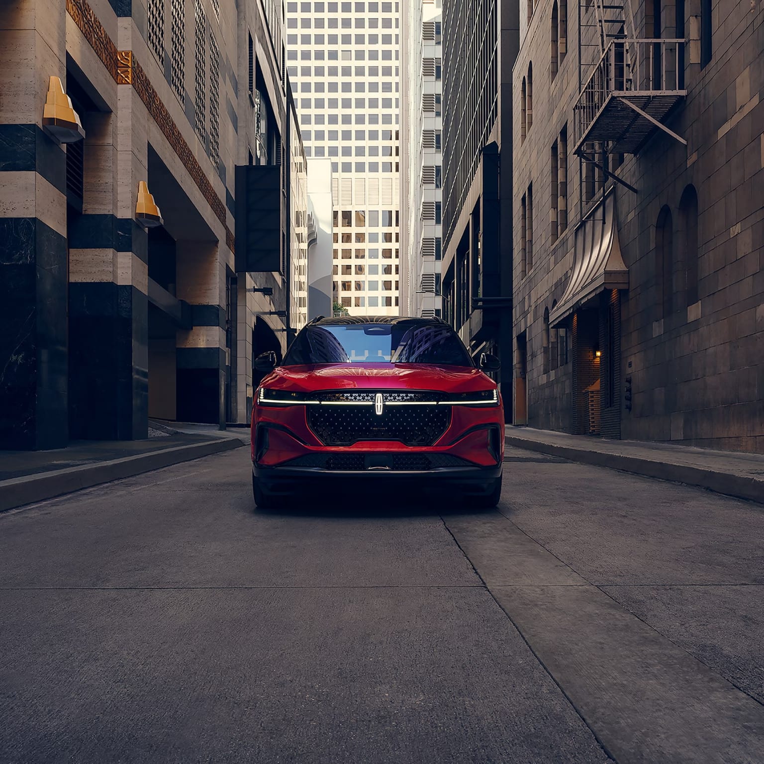A sleek, red sports car parked in a narrow city street with towering skyscrapers and a dimly lit urban landscape.