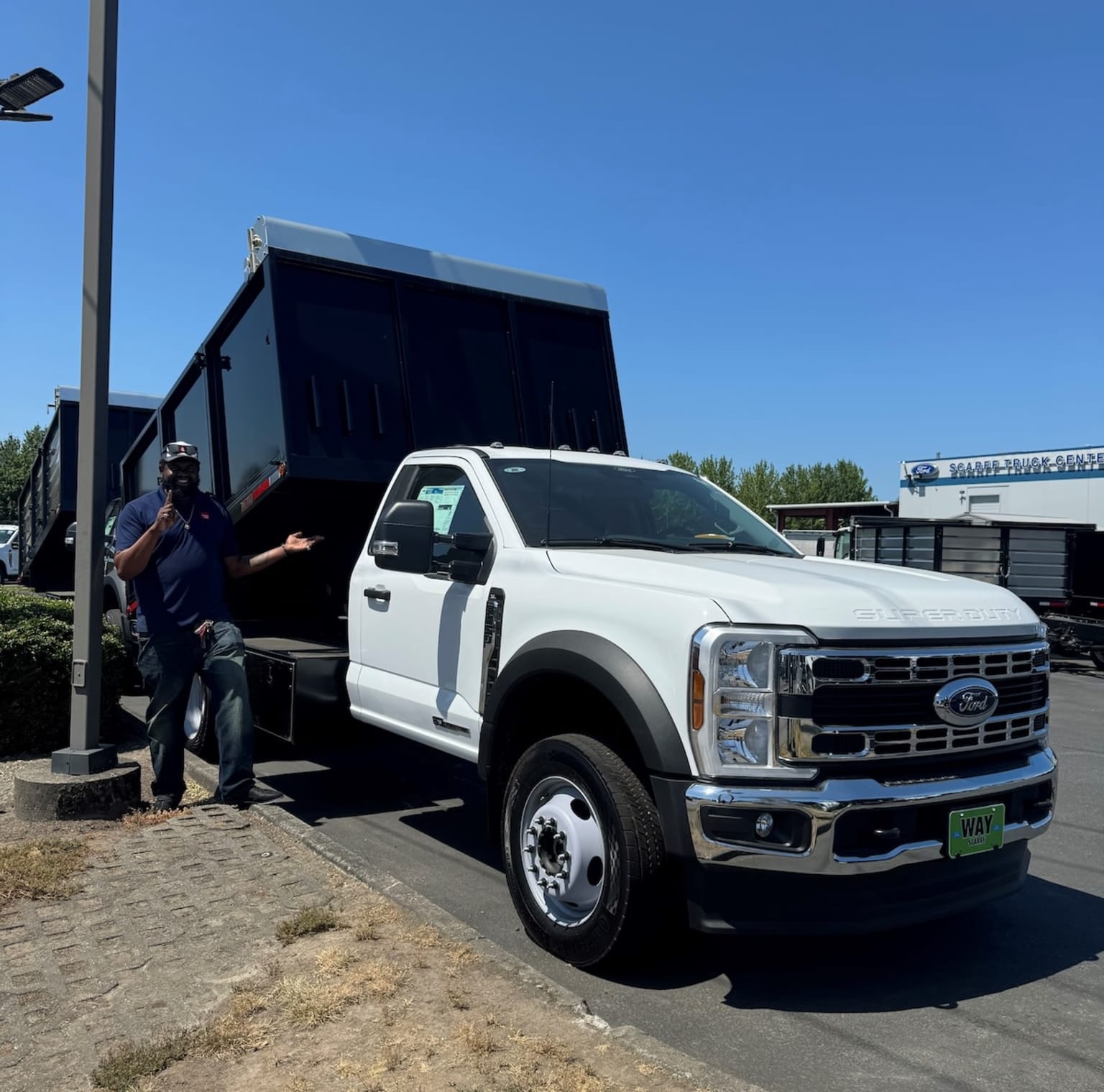 A large white truck with a black dump bed is parked in front of a building, with a clear blue sky in the background.