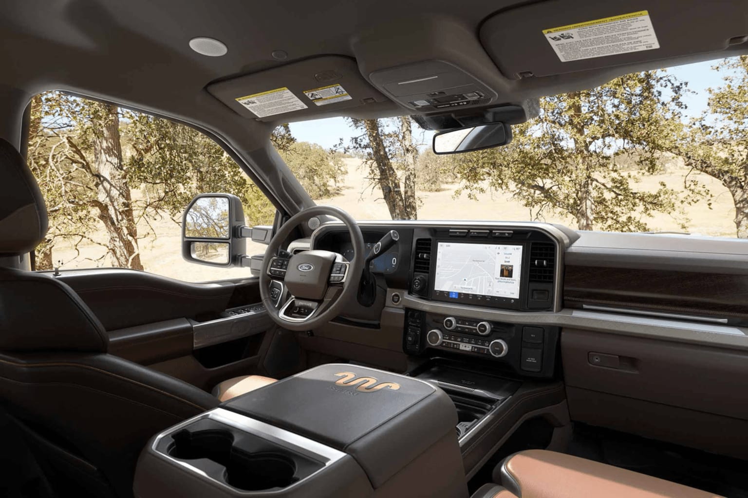 Interior of a vehicle with dashboard display and steering wheel visible, surrounded by a natural outdoor landscape with trees and foliage in the background.