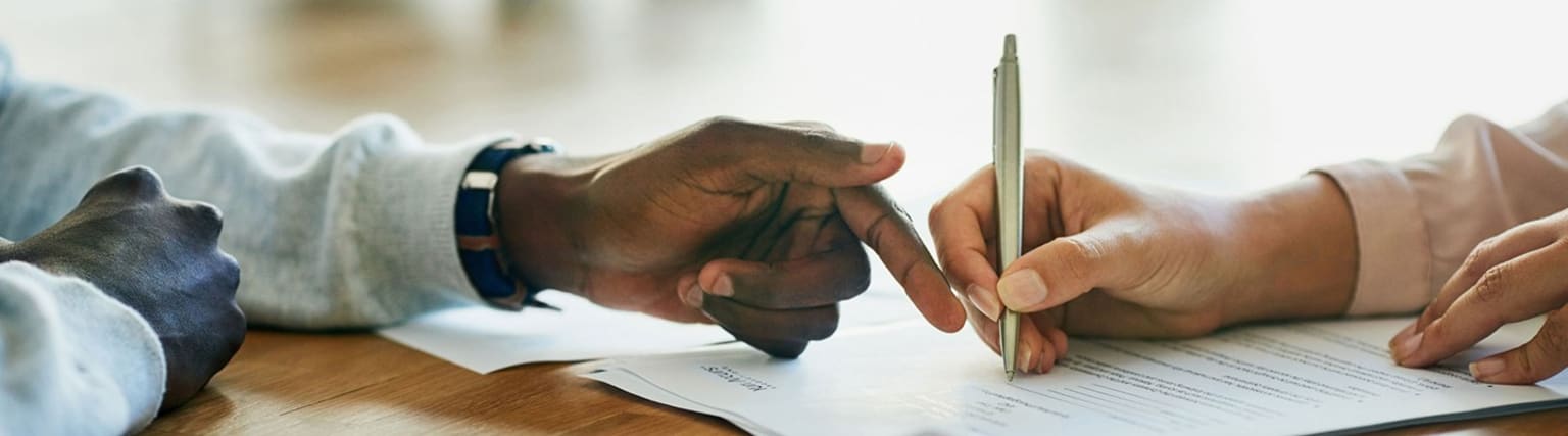 A person's hands are shown on a desk, with one hand holding a pen and the other covering the face, suggesting a moment of contemplation or frustration.