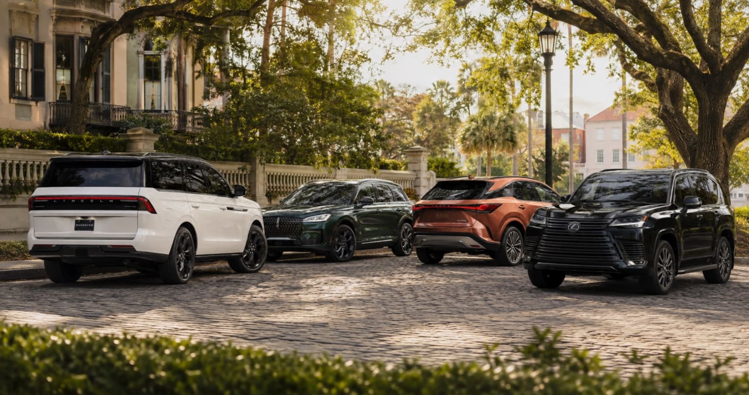 Luxury SUVs parked on cobblestone street in front of historic building and trees