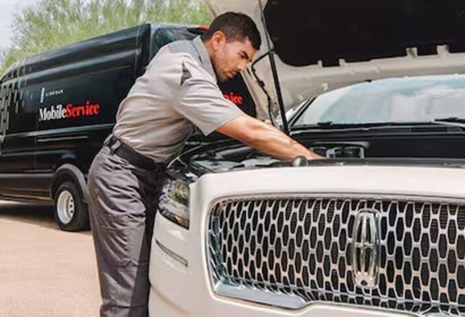 A man in a uniform is working on the front of a large white truck with a Mobile Unite logo on the side.