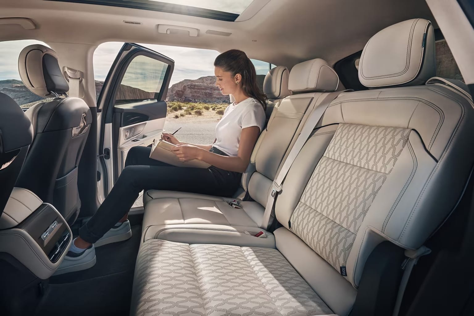 Interior of a vehicle with a person reading a book in the backseat against a scenic landscape.