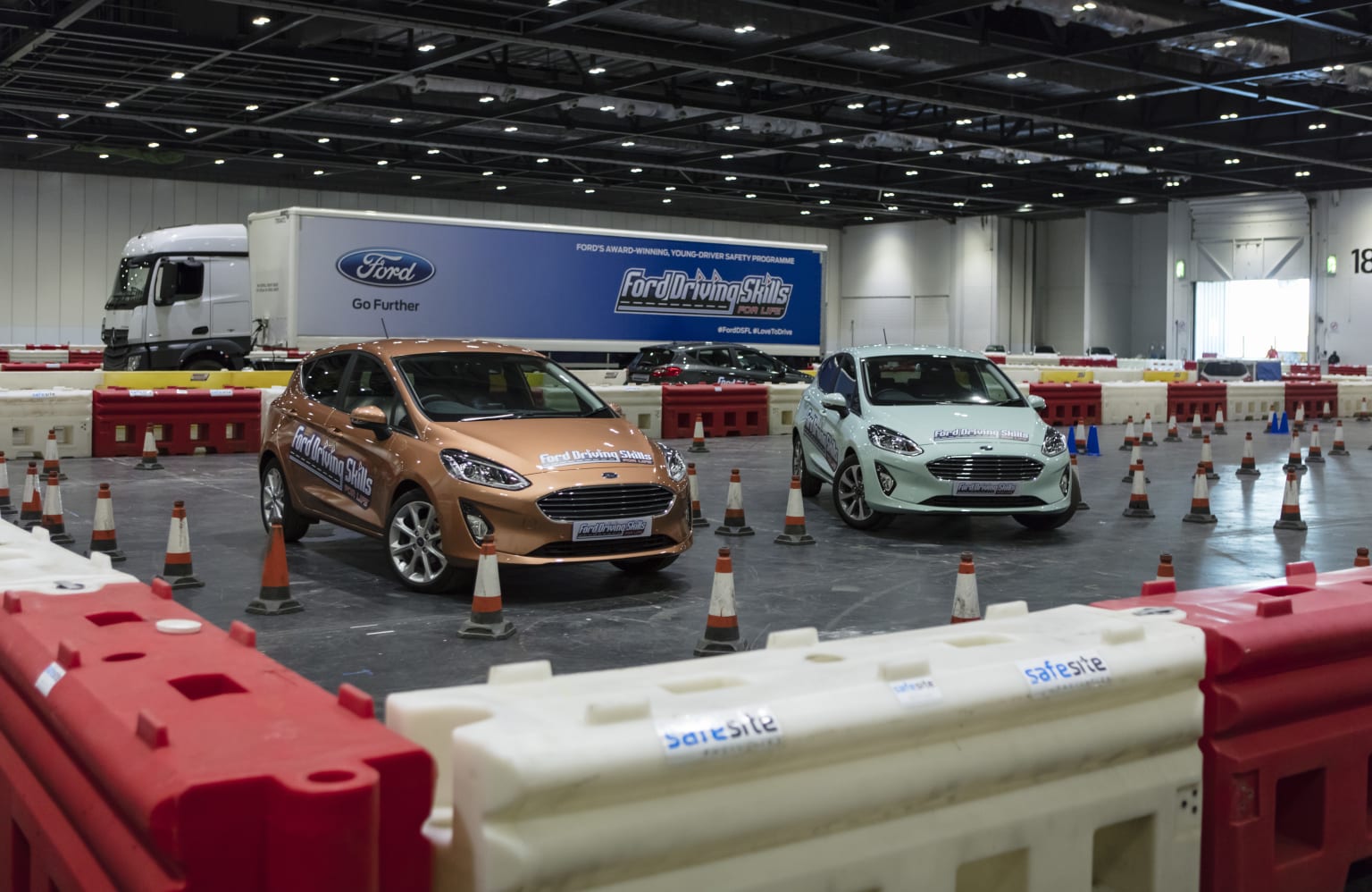 a group of cars parked next to each other in a building with orange and white barriers around them and a blue and white truck in the background