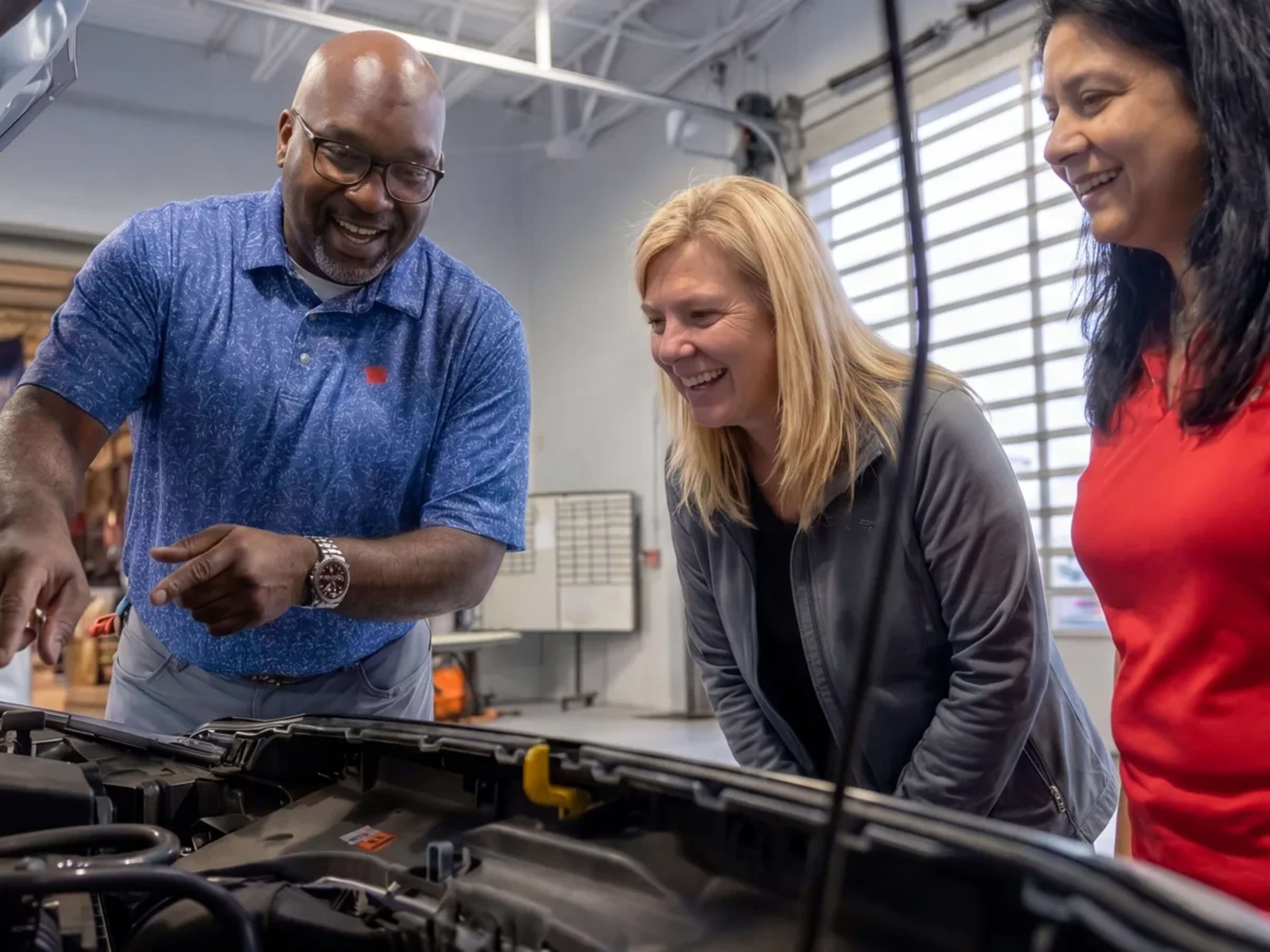 Apple Ford service advisor showing two customers under-hood details on their vehicle inside the service bay