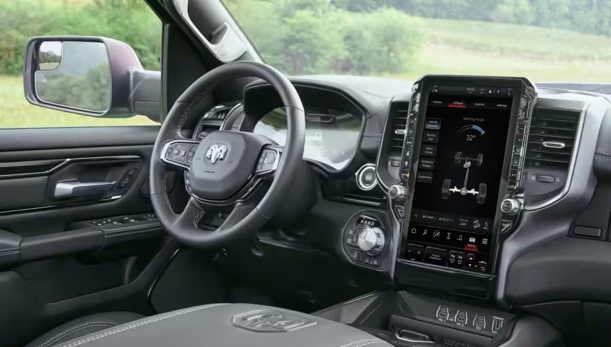 Truck interior with leather steering wheel and digital infotainment screen, overlooking green landscape.