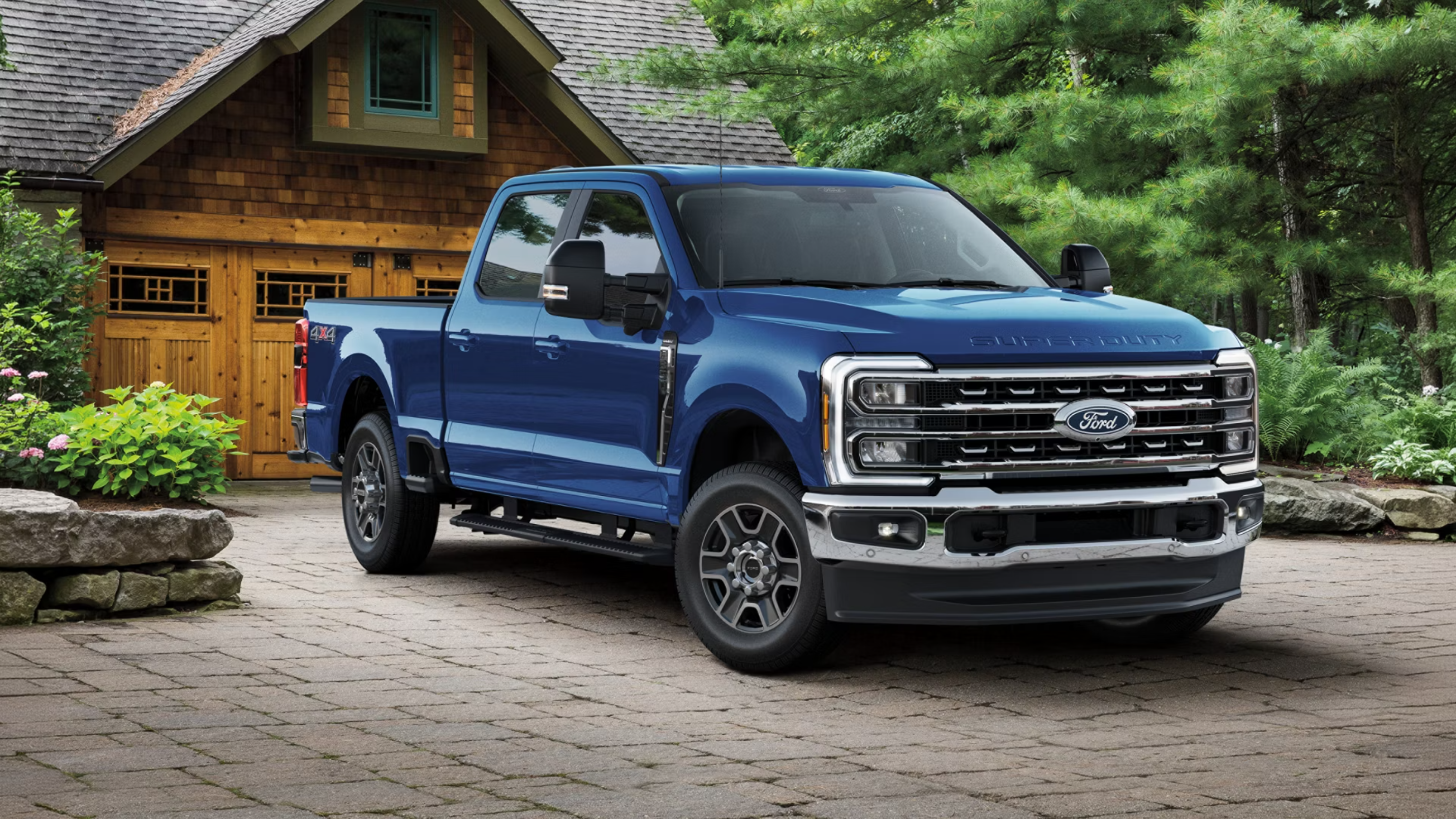 Blue pickup truck parked on stone driveway in front of rustic wooden house and trees.