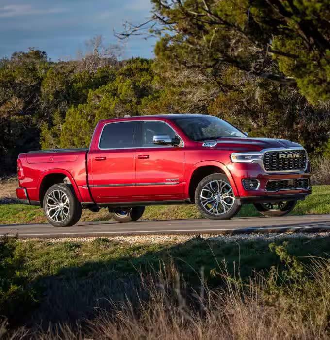 A red pickup truck parked on a paved path with grass and trees in the background.