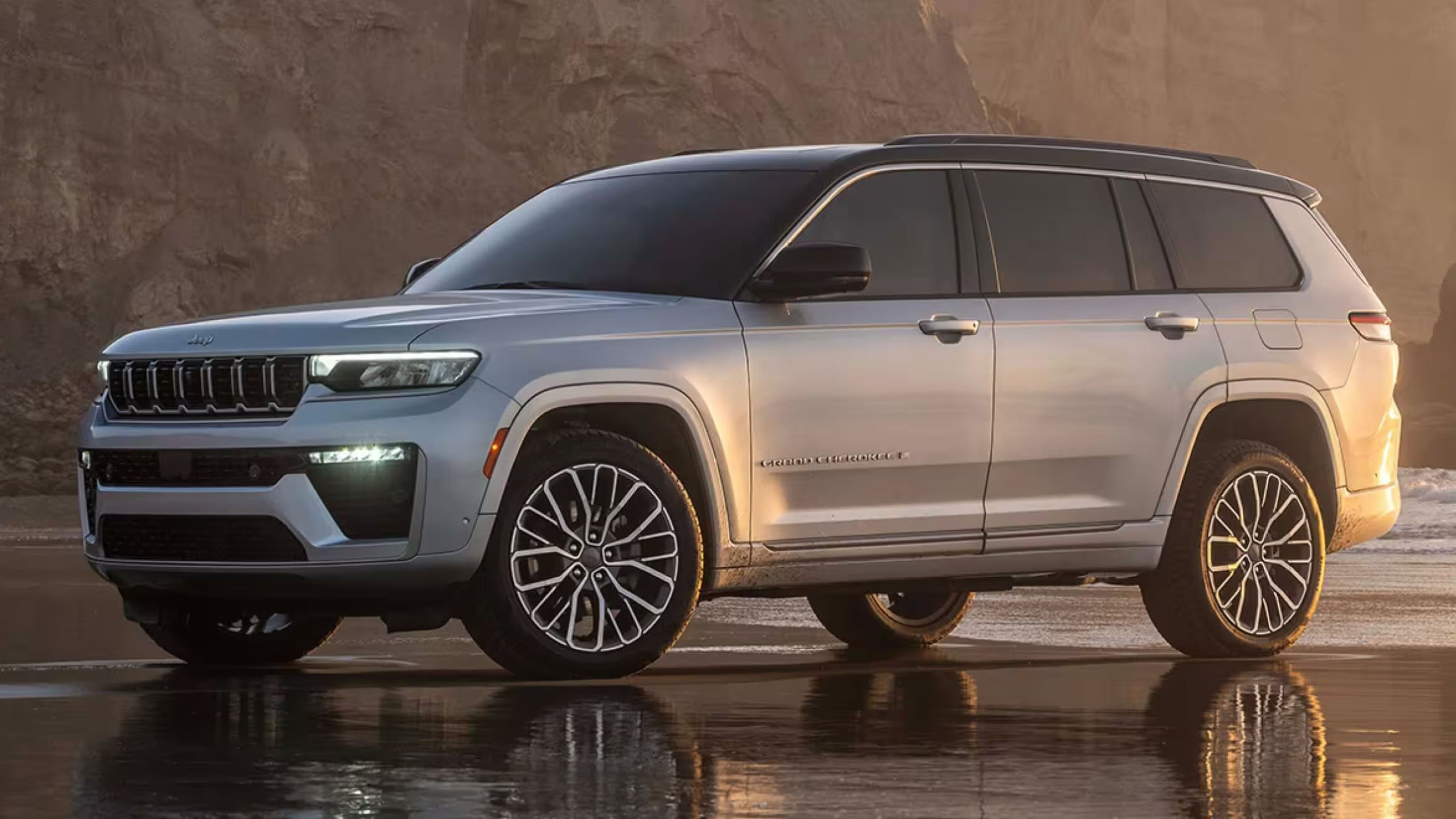A silver SUV is parked on a wet sandy beach with a rocky cliff face in the background.