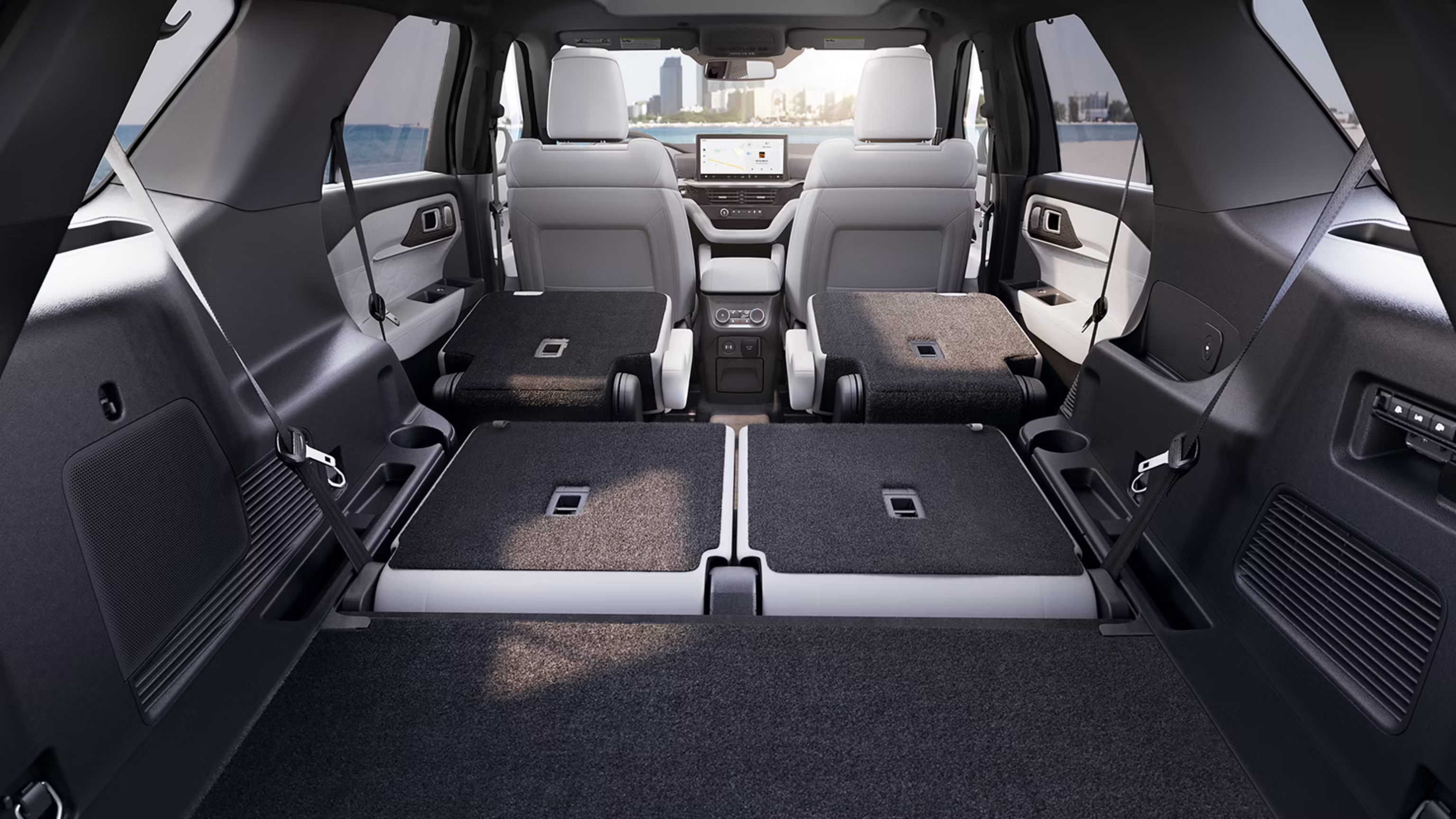 Vehicle interior with folded rear seats and city skyline visible through the windshield.